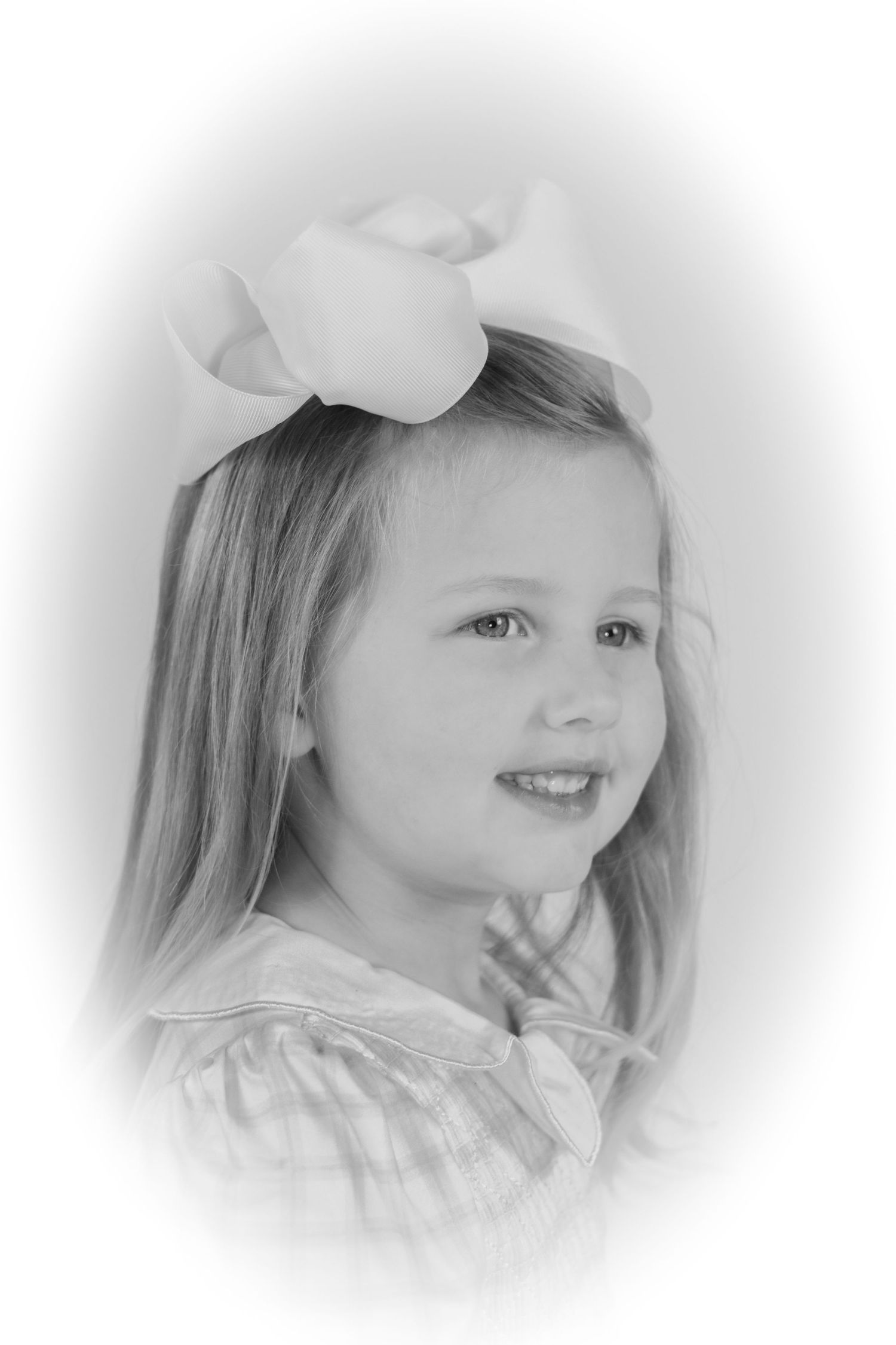 Black and white portrait of a young girl with long hair and oversized white bow, smiling softly.