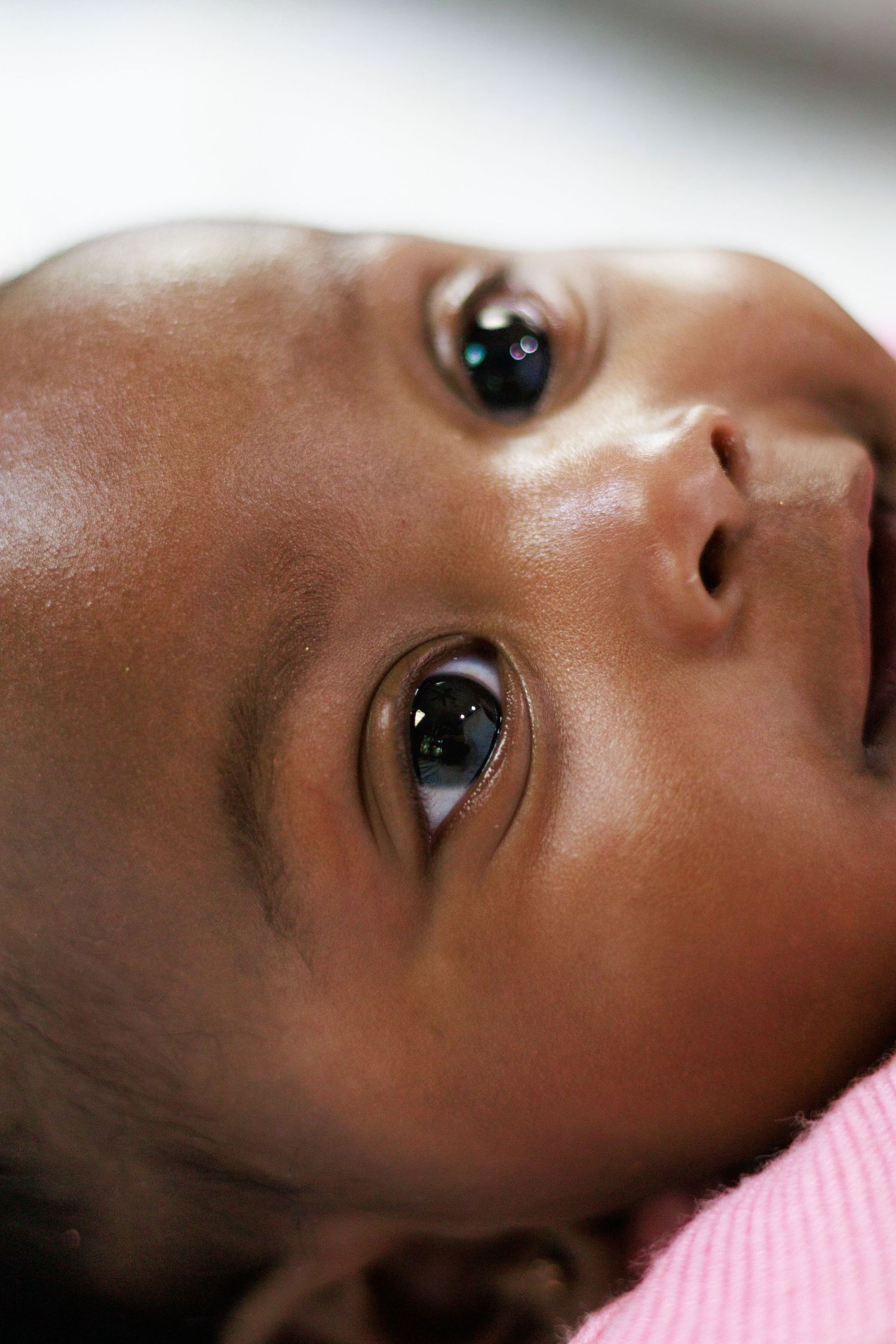 Close-up portrait of a newborn baby with bright eyes looking upward wearing pink.