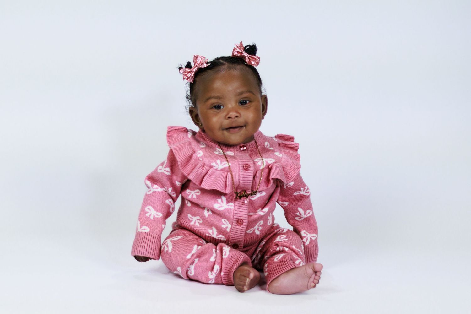 Happy baby girl in pink floral ruffled romper with bow pigtails smiling on white background.