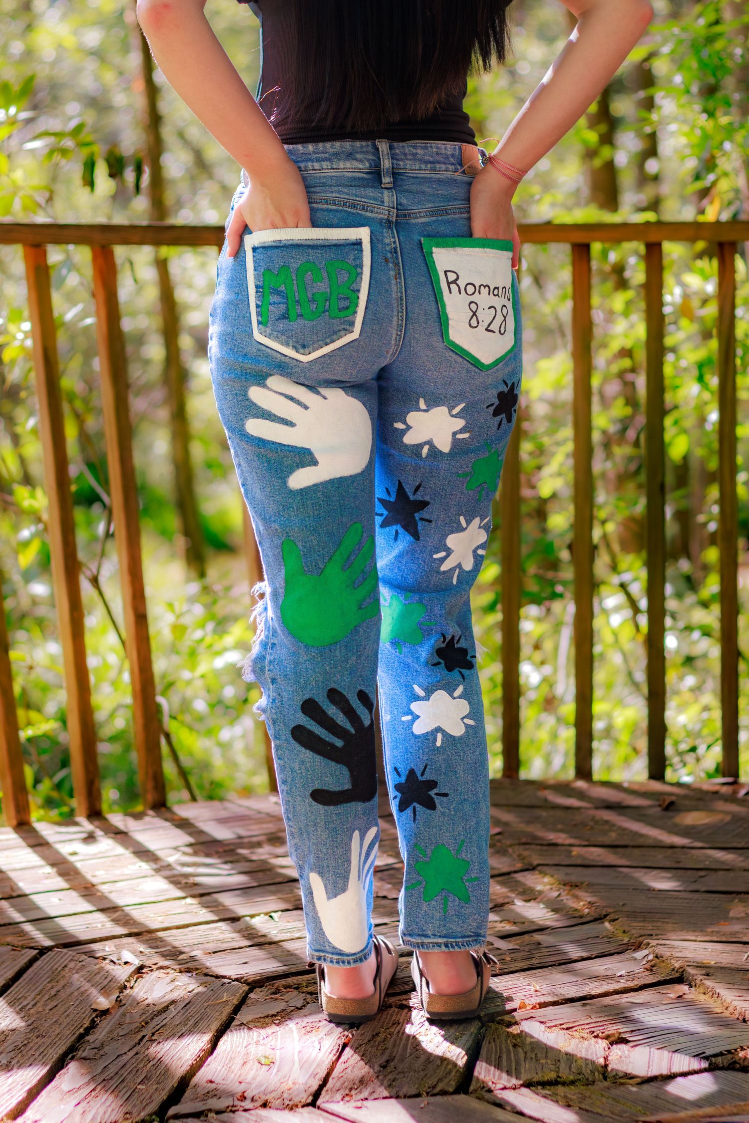 Custom painted jeans featuring hand prints, paint splats, and Romans 8:28 Bible verse on back pockets.