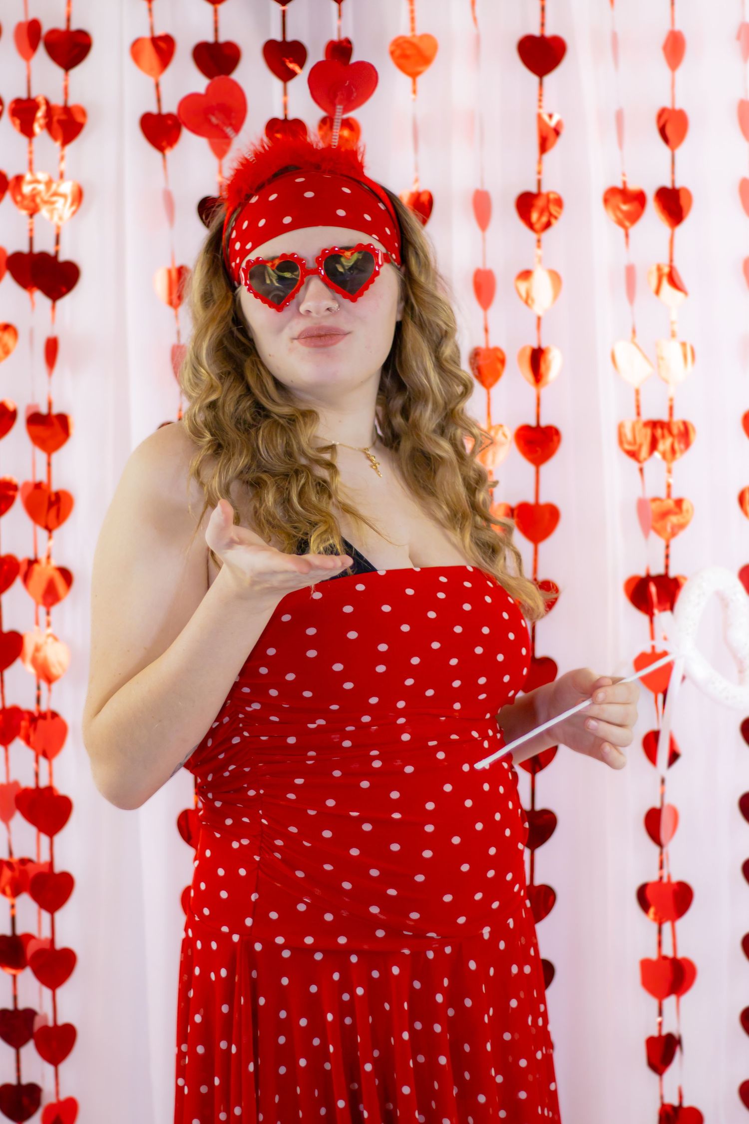 Woman in red polka dot dress wearing heart-shaped sunglasses holding a card near heart garlands.