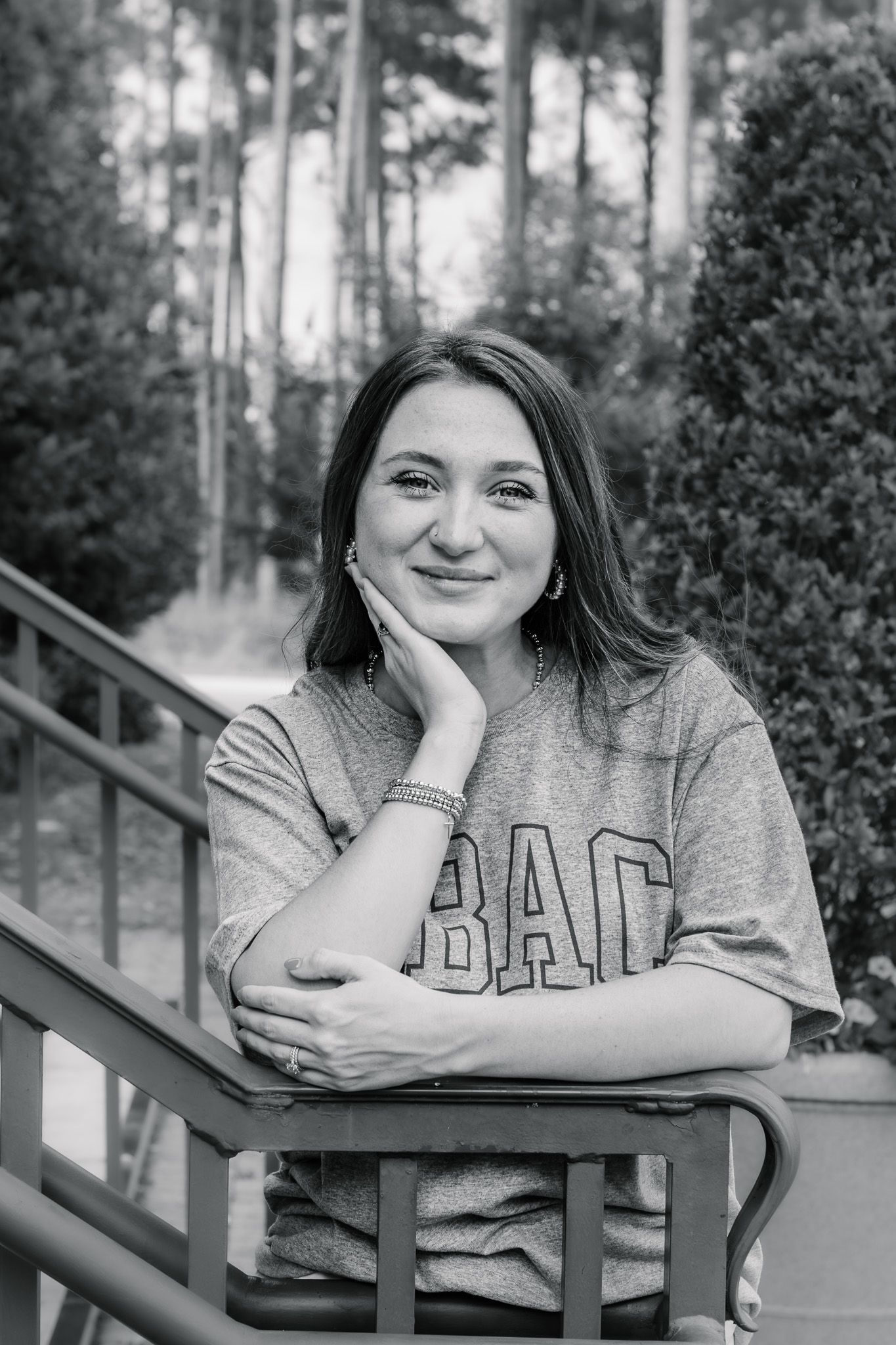 Black and white portrait of smiling young woman leaning on railing outdoors.
