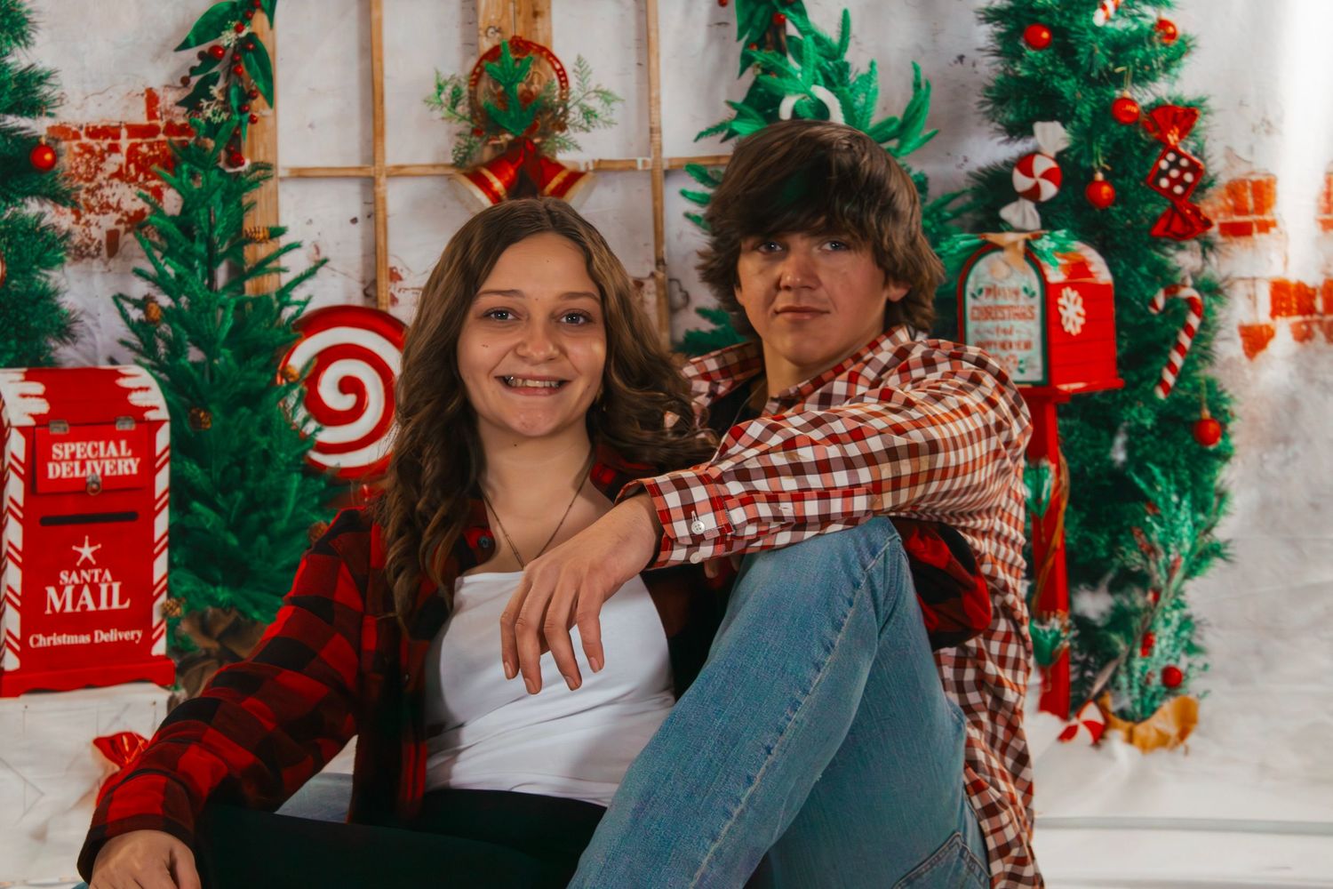 Teen boy and girl sitting together smiling in front of colorful Christmas holiday backdrop.