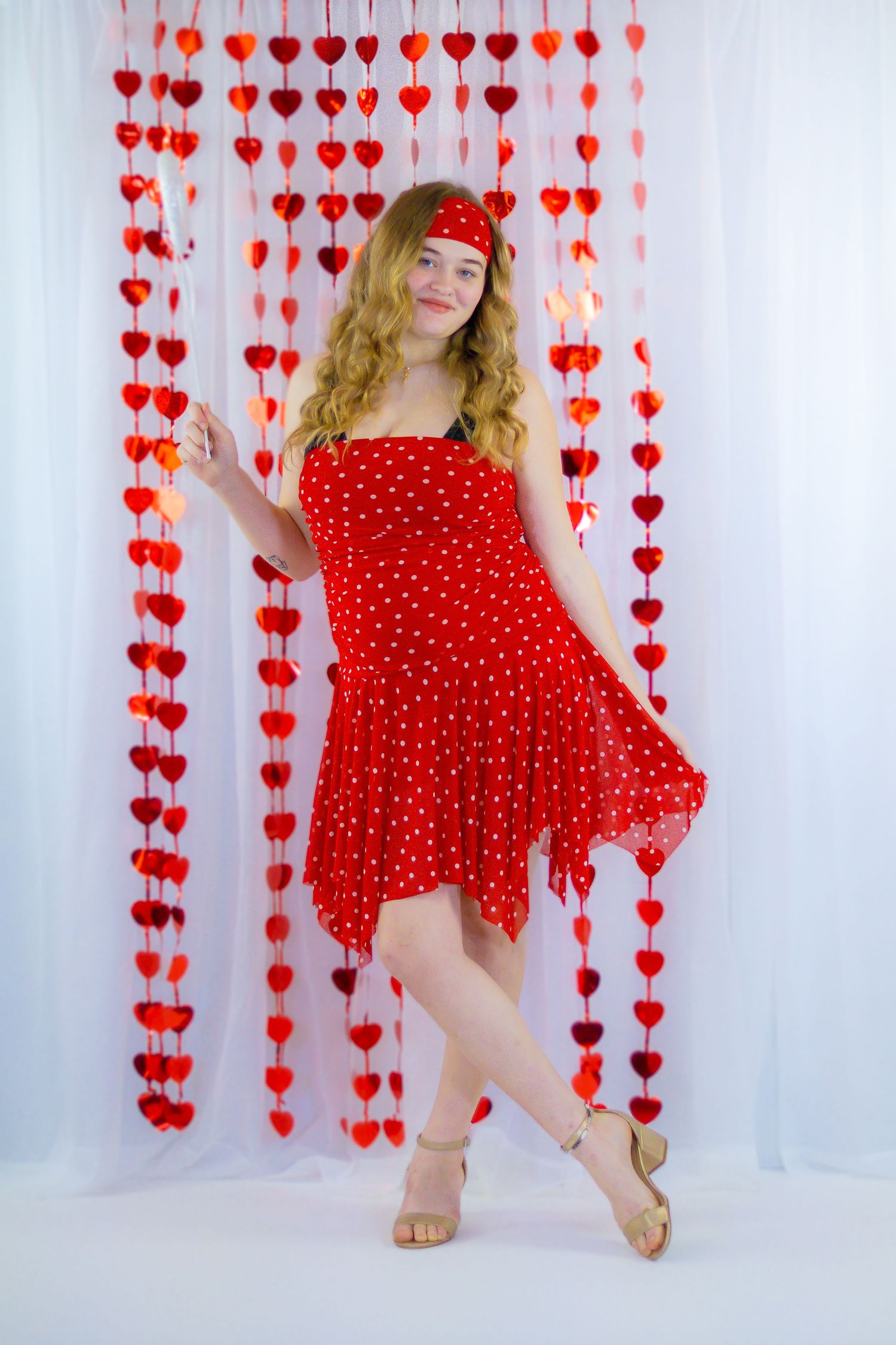 Woman in red polka dot dress posing beside red heart garland curtains.