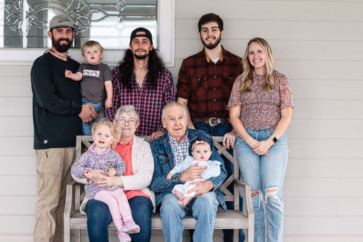 Multi-generational family portrait of grandparents with grandchildren on a porch bench.