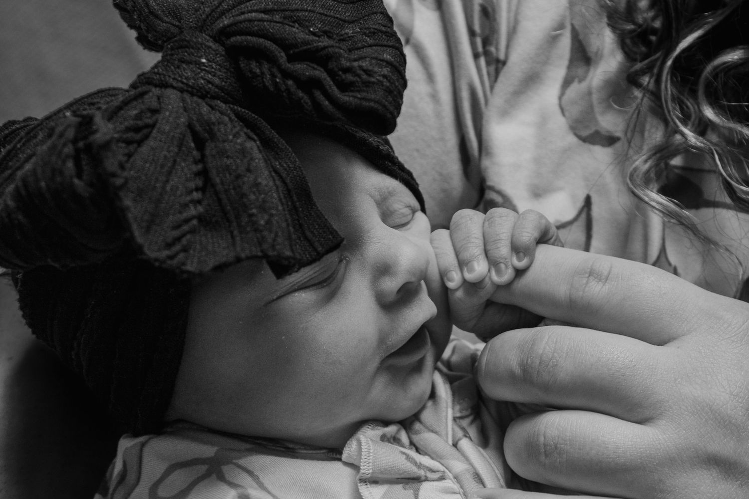 Black and white close-up of sleeping newborn baby gripping mothers finger.