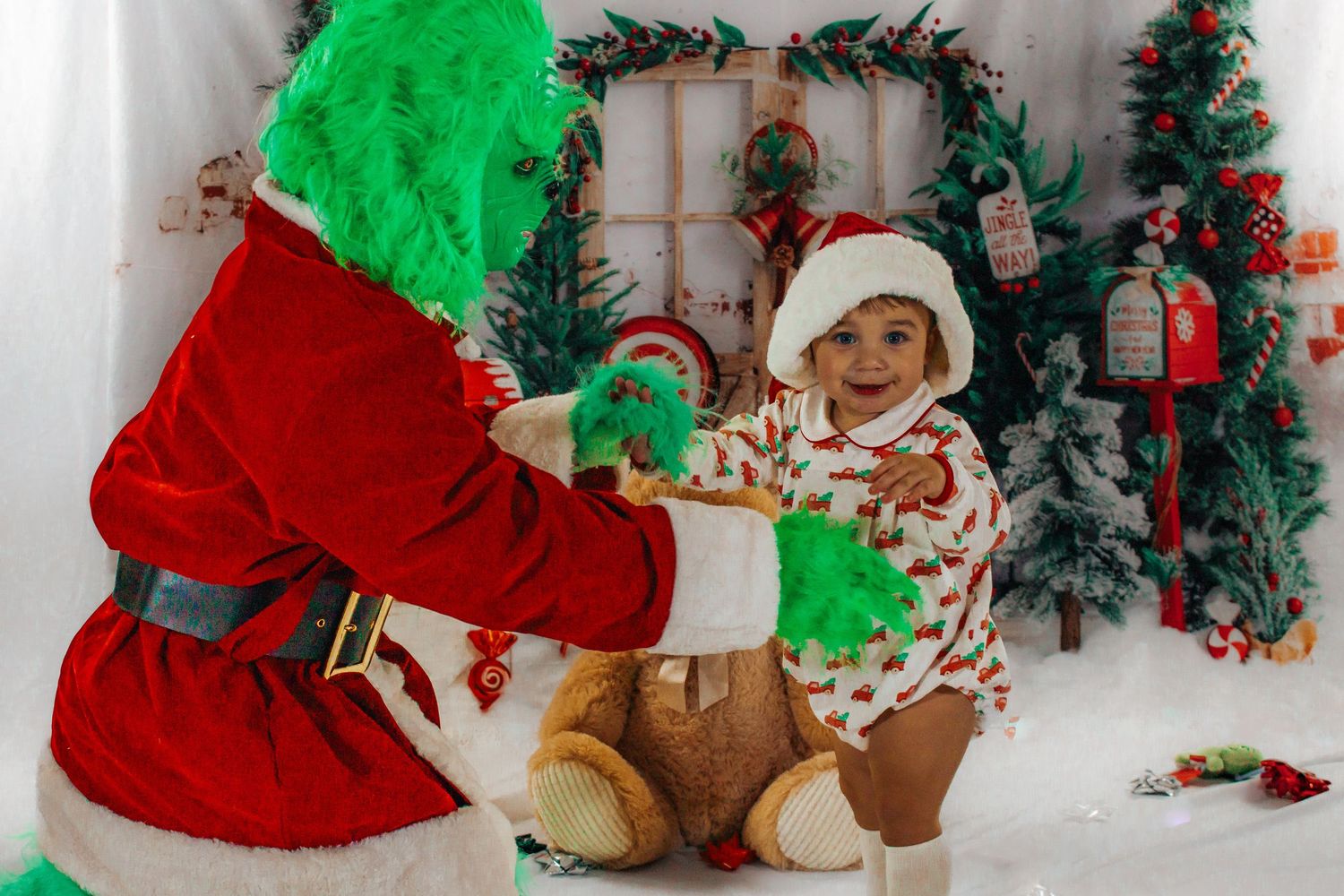 Baby in Christmas onesie and Santa hat held by the Grinch character in a decorated holiday photo set.