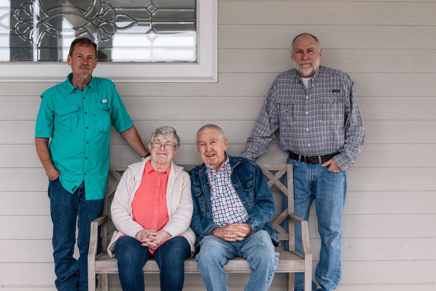 Four adults pose on a porch bench, two standing and two seated, smiling for a family portrait.