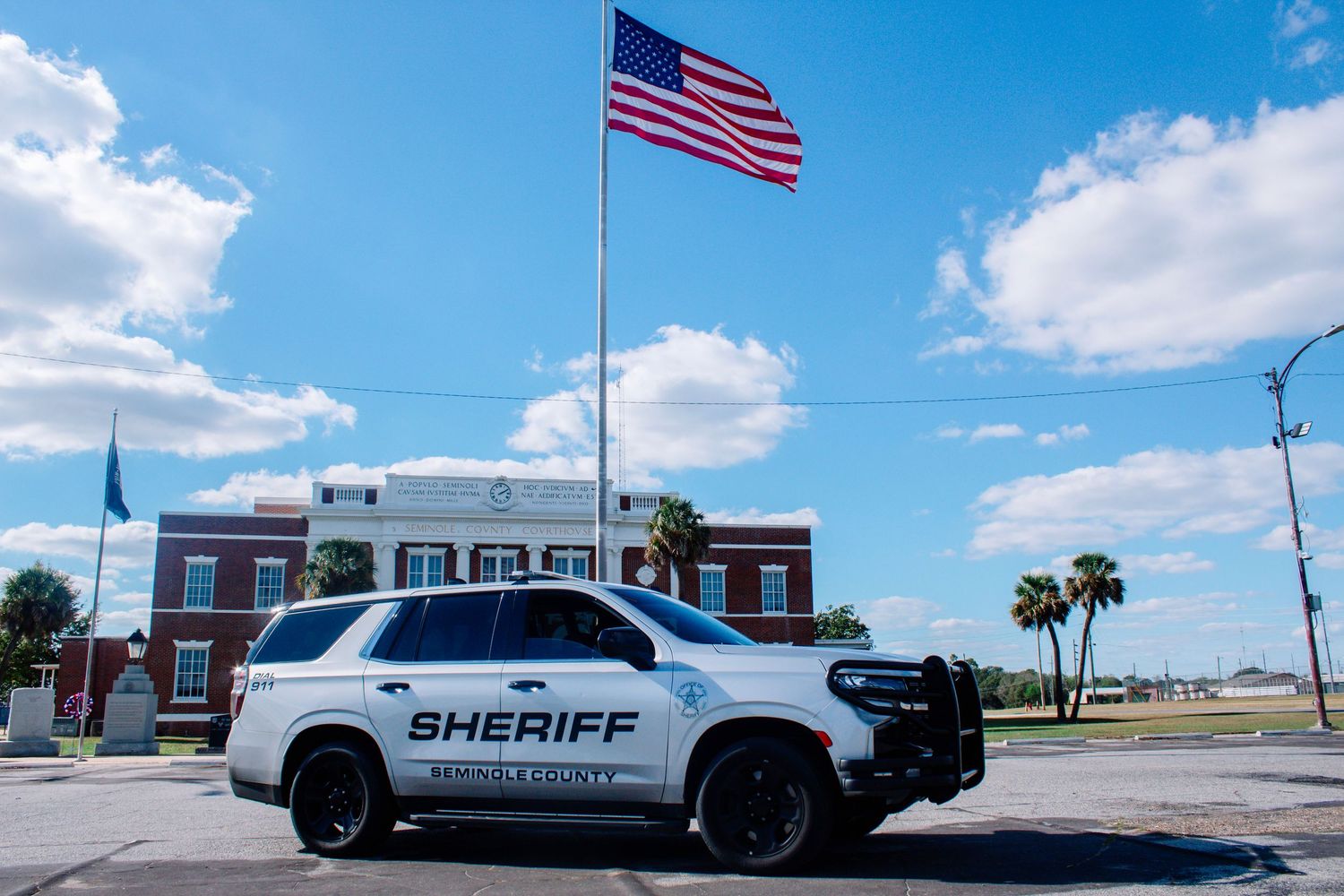 Okeechobee County Sheriff SUV parked near flagpole with American flag against blue sky.