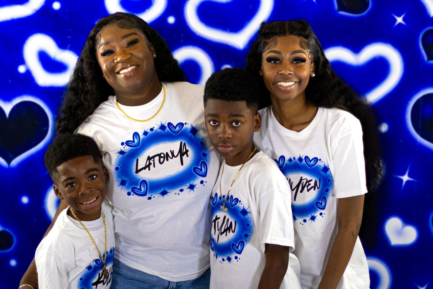 Family of four wearing matching custom name shirts posing in front of a blue heart backdrop.
