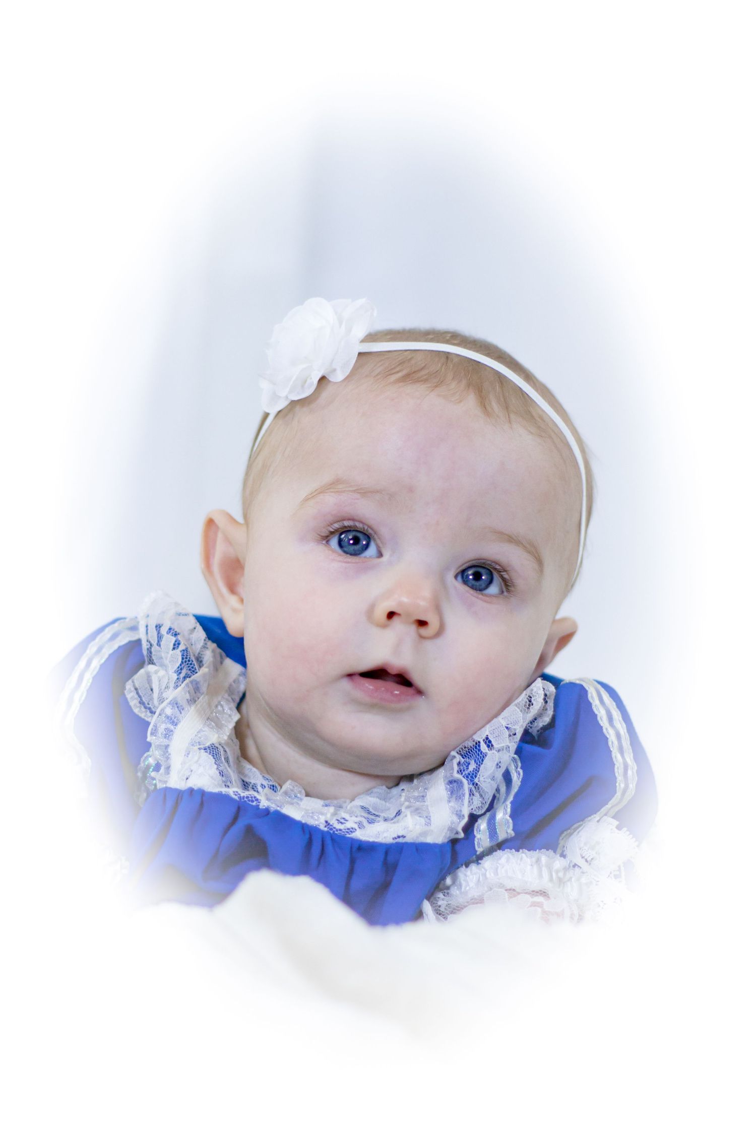 Close-up portrait of a baby girl with blue eyes wearing a blue lace dress and white flower headband.