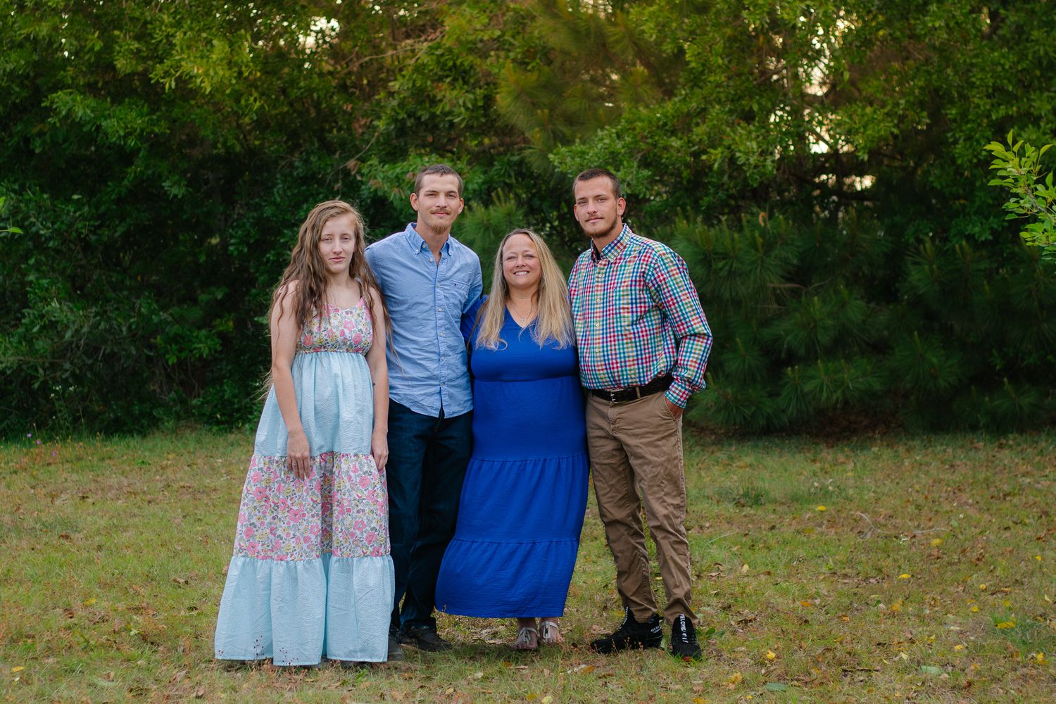 Family of four posing together outdoors in a lush green park during a photo session.