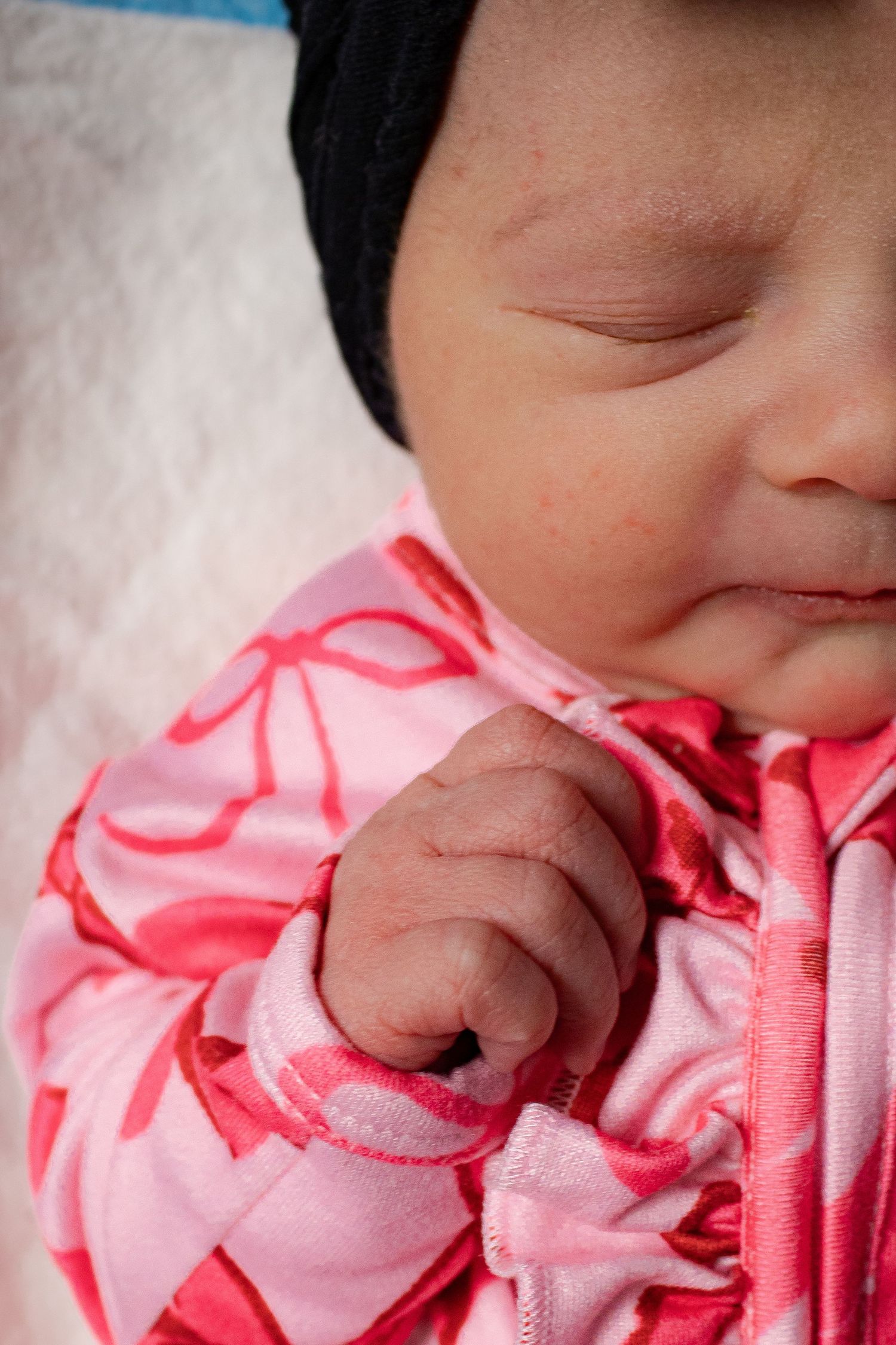 Sleeping newborn baby girl in pink bow onesie and black headband wrap.