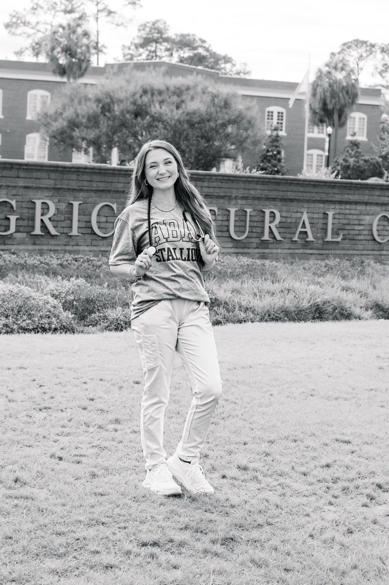 Smiling young woman in college sweatshirt poses near agricultural college sign in black and white.