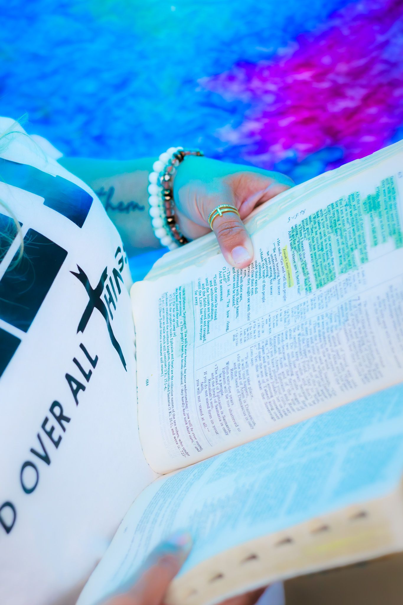 Close-up of highlighted Bible pages held by woman wearing bracelet near stained glass.