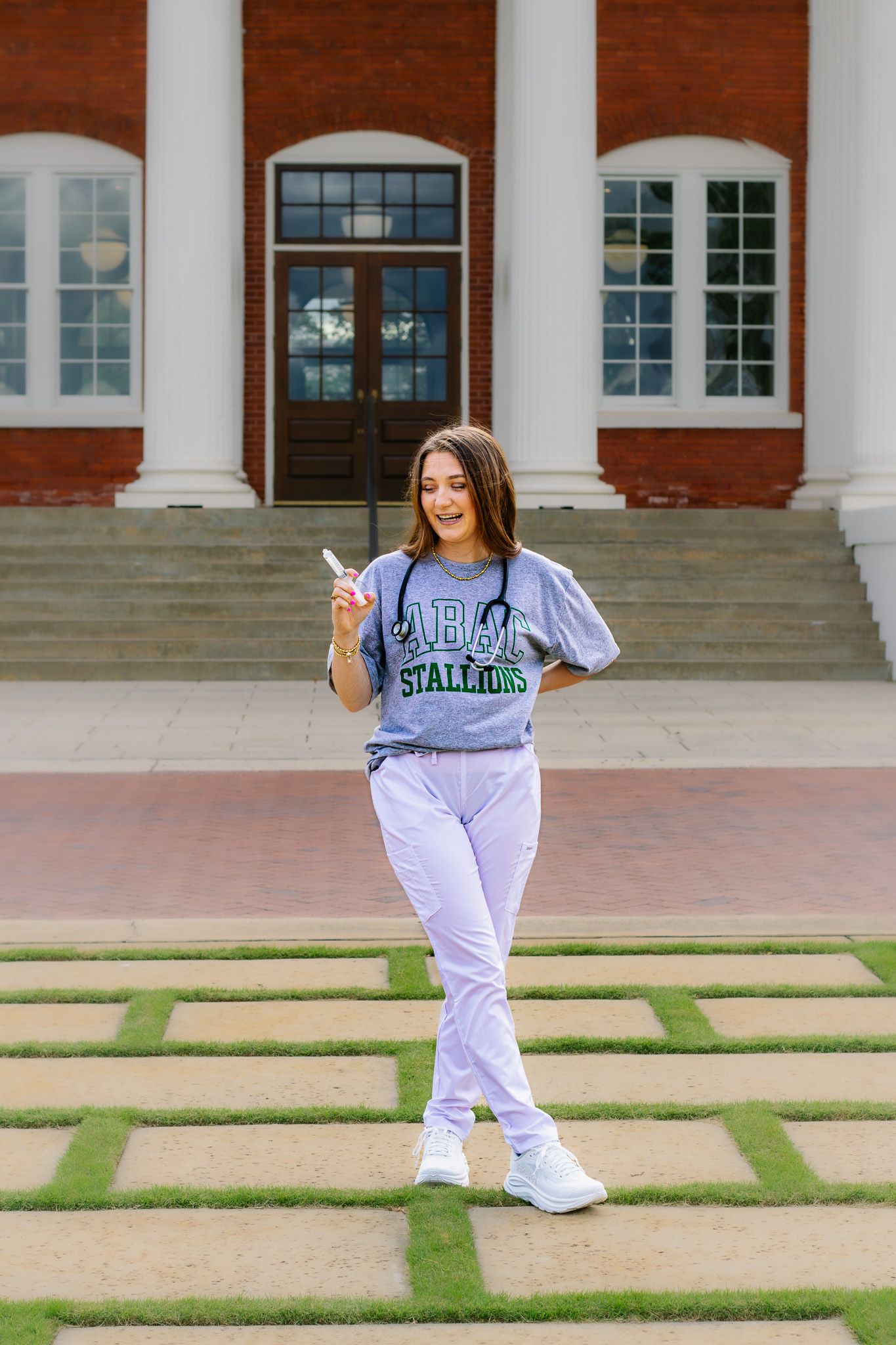 Young woman in college sweatshirt and lavender pants walks outside classic brick building.