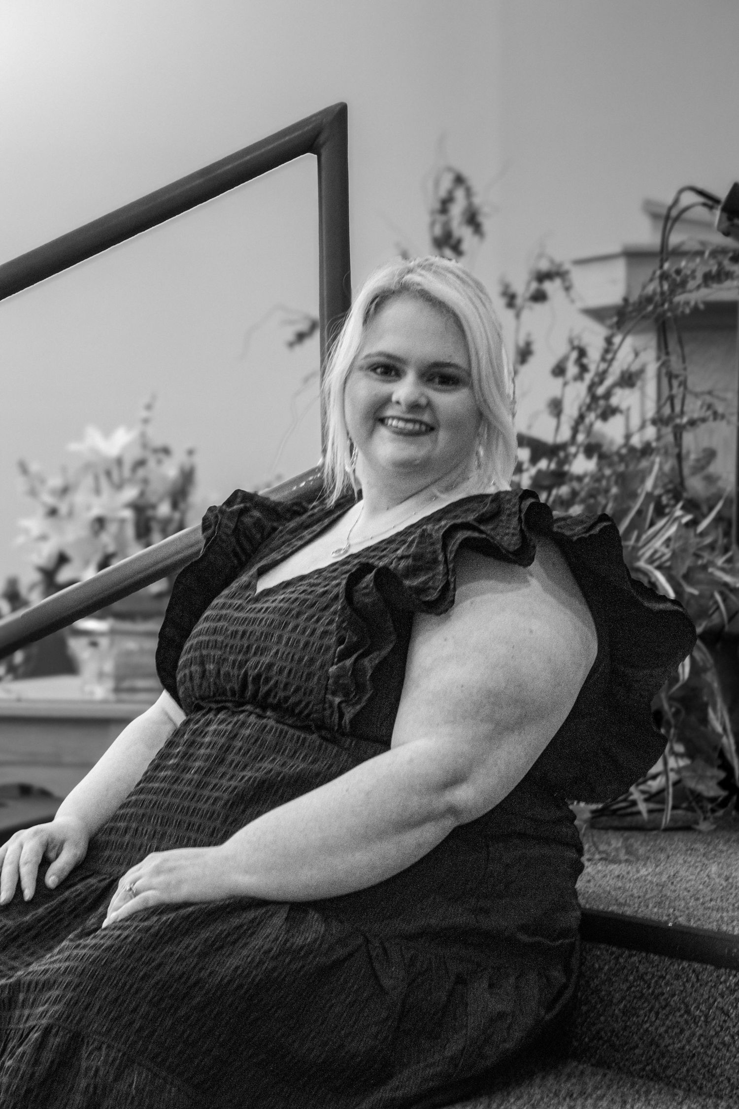 Black and white portrait of smiling blonde woman in black dress seated on church steps.
