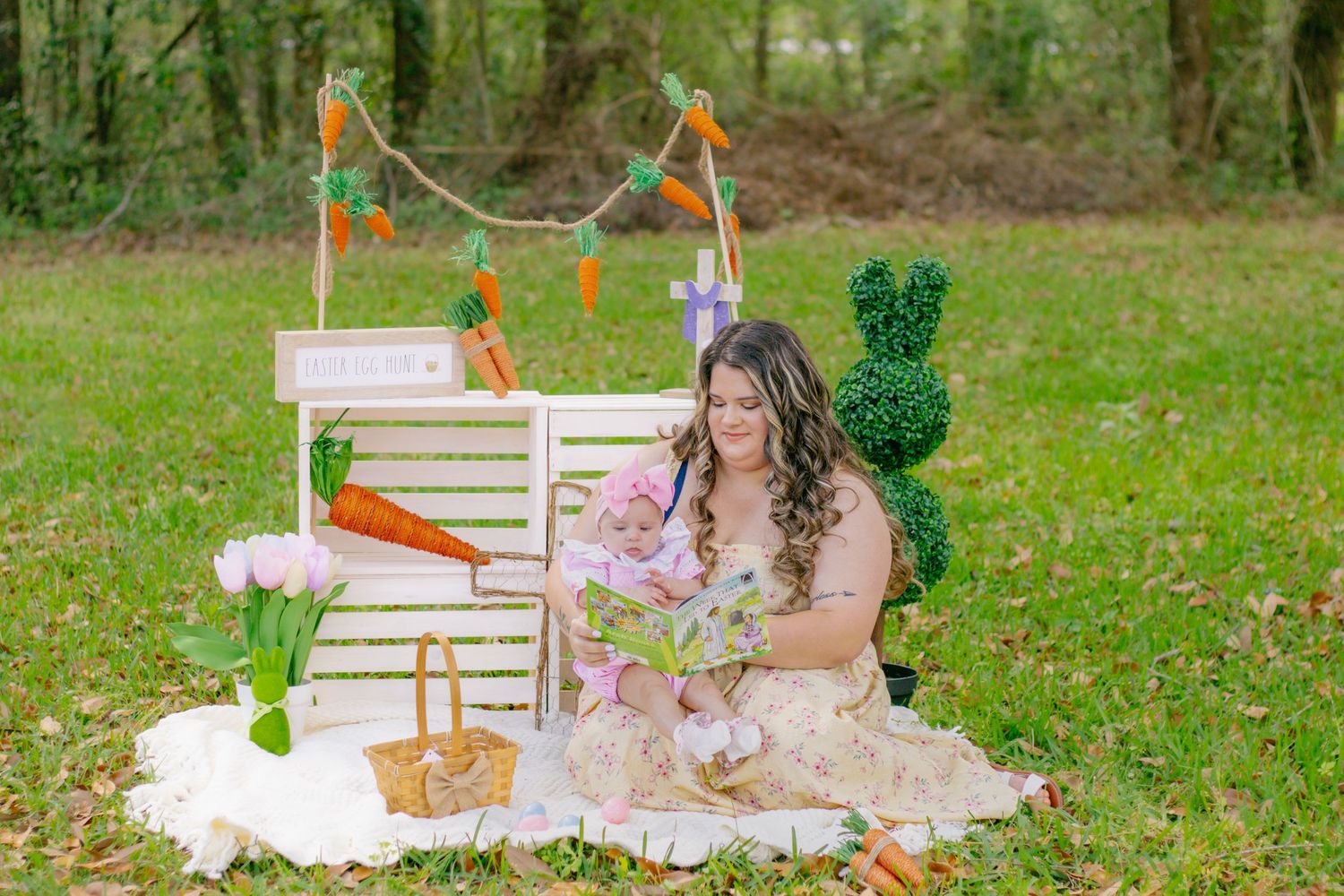 Woman in floral dress sitting on blanket with Easter decorations including carrots and white crates outdoors.