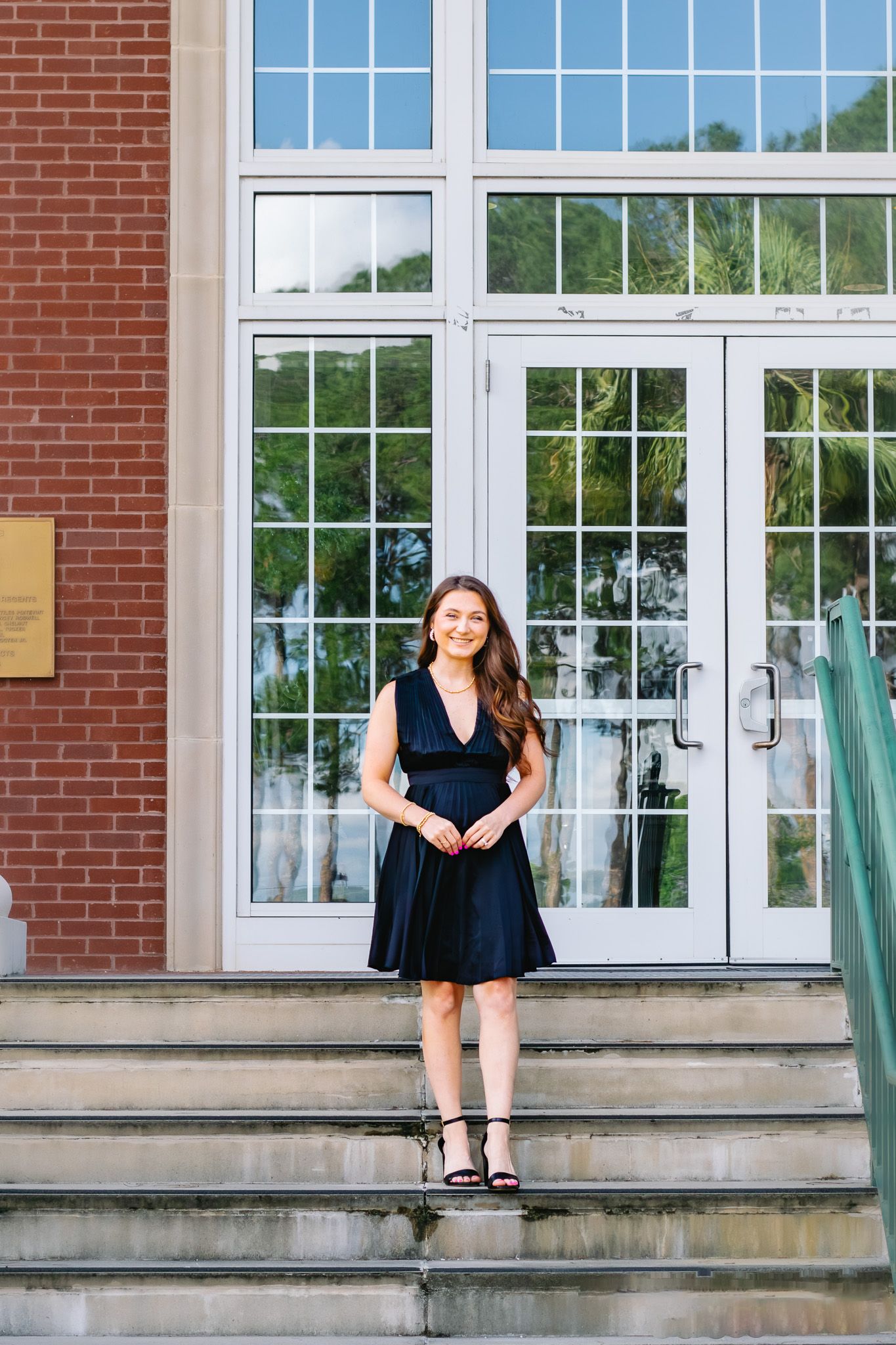 Smiling woman in black dress standing on steps outside brick building.