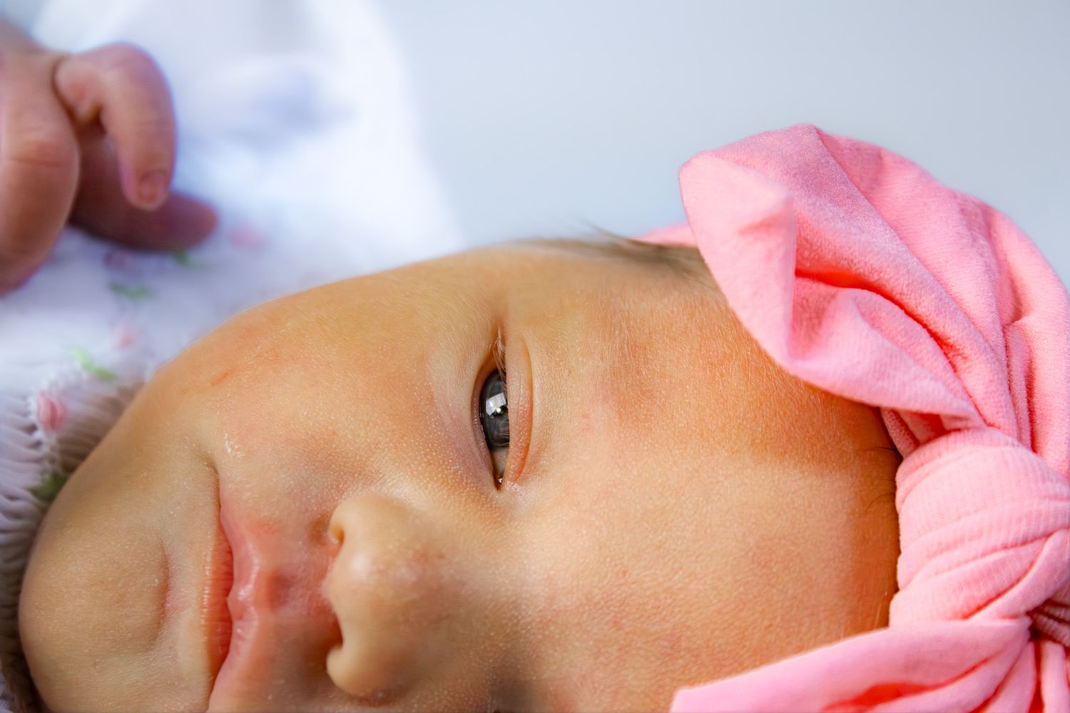 Close-up portrait of a sleeping newborn baby girl wearing a pink bow headband.