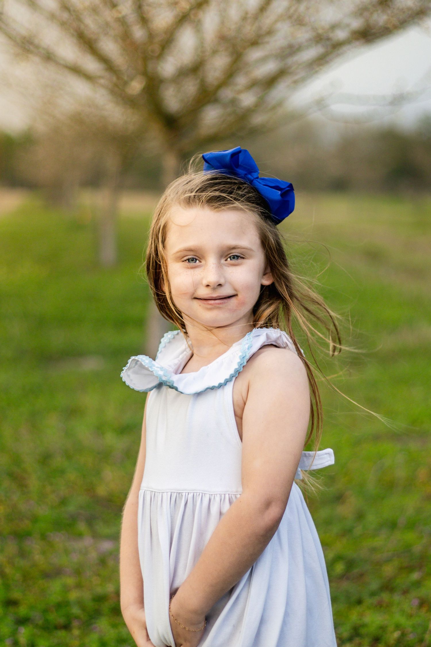 Young girl in white dress with blue bow smiling in green field.