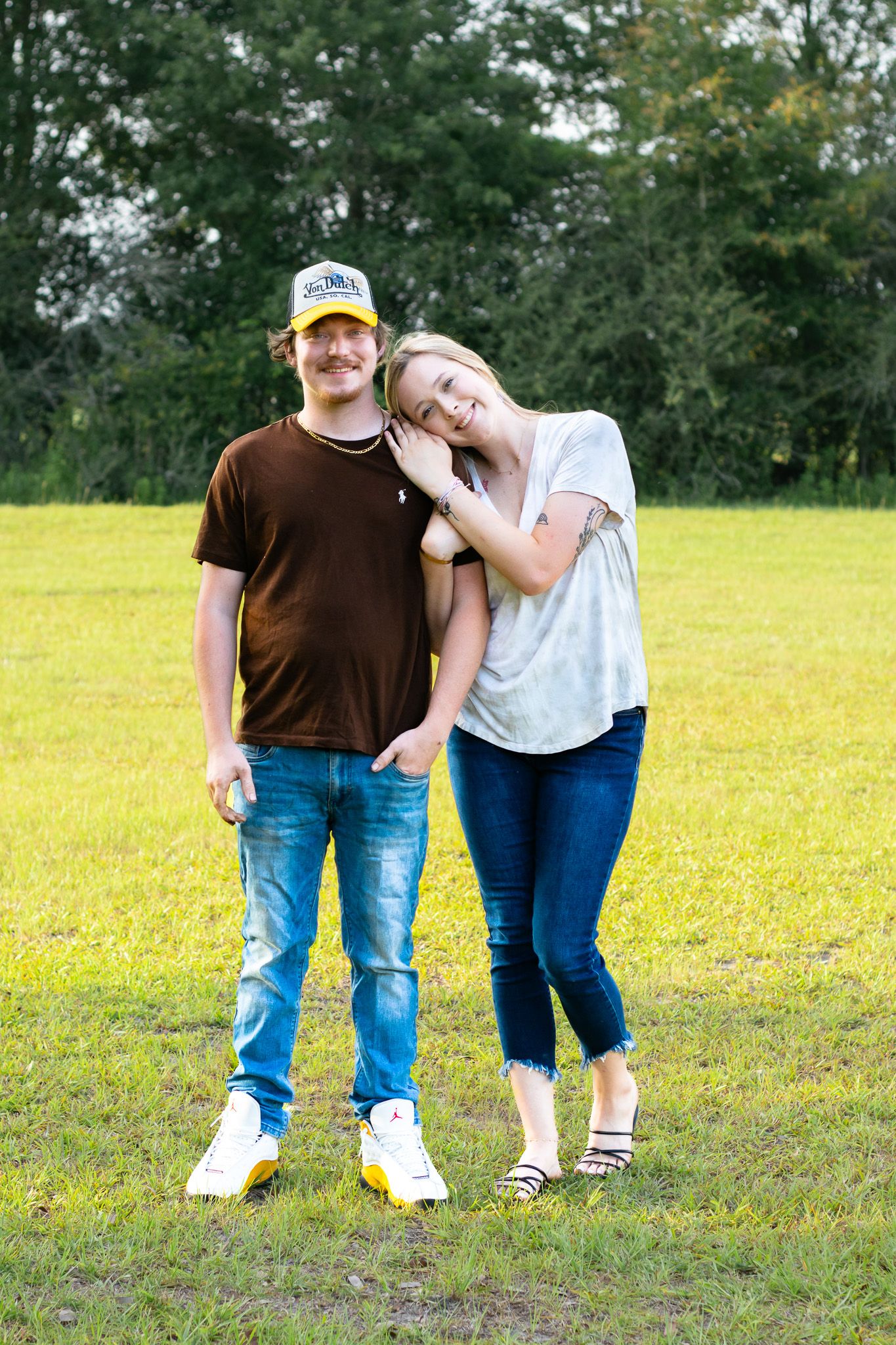 Young couple standing together on green grass field, woman leaning on mans shoulder smiling.