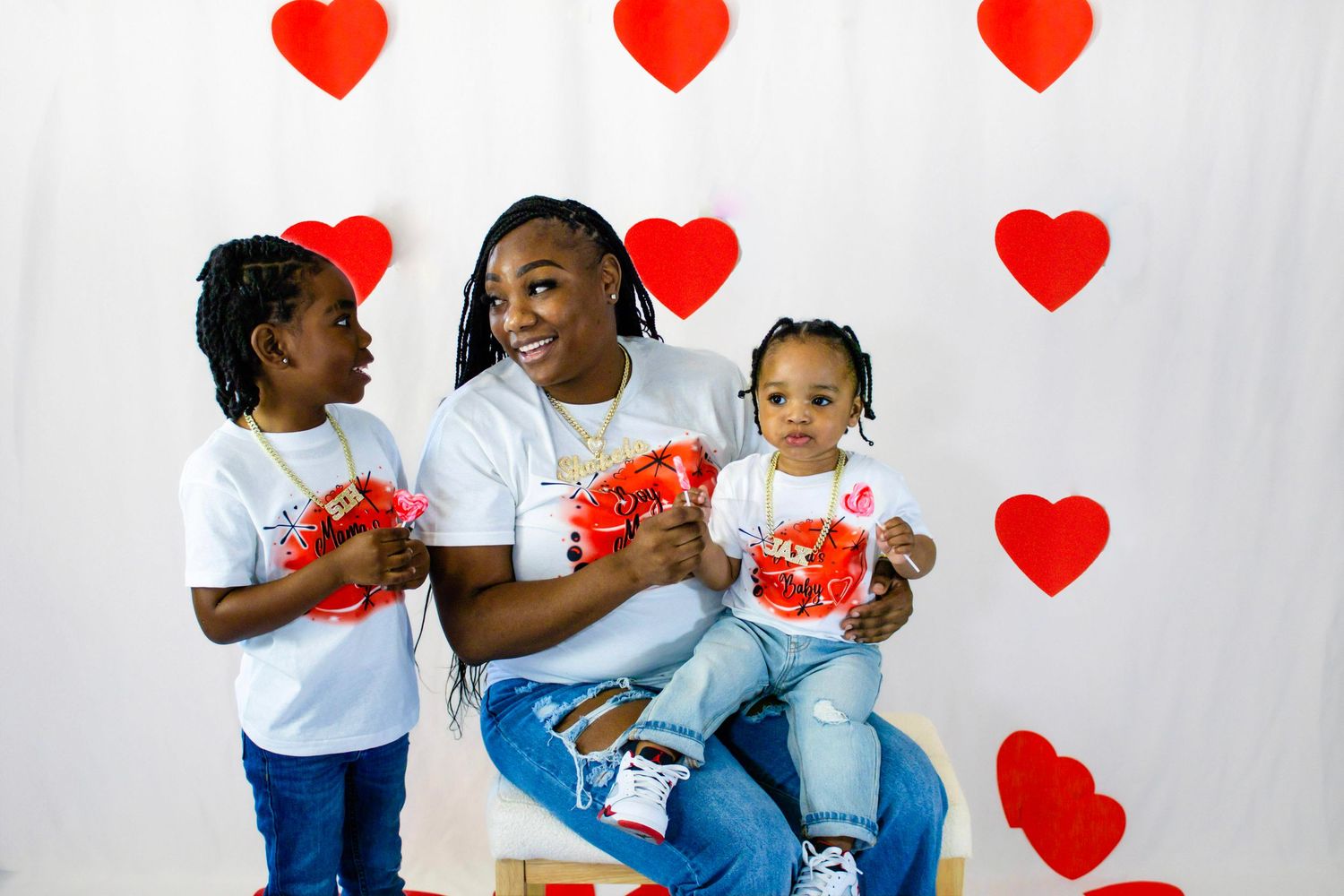 Mom with two kids holding Valentine's Day gifts in front of white backdrop with red heart decorations.
