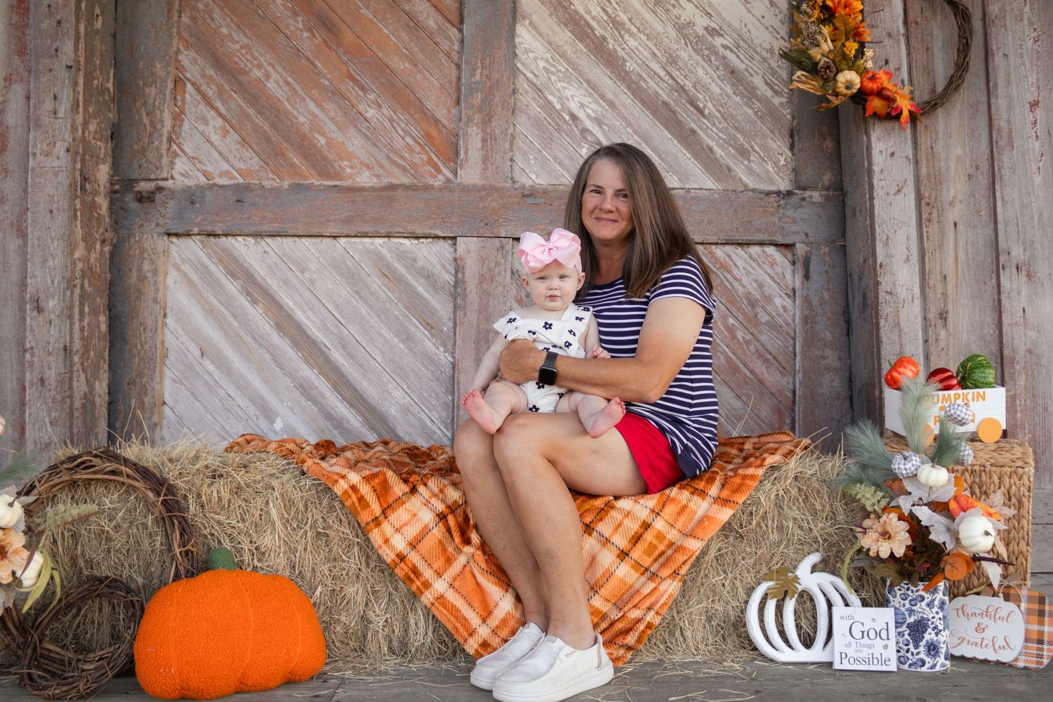 Woman holding baby girl in dalmatian outfit on hay bale with fall pumpkin decor.