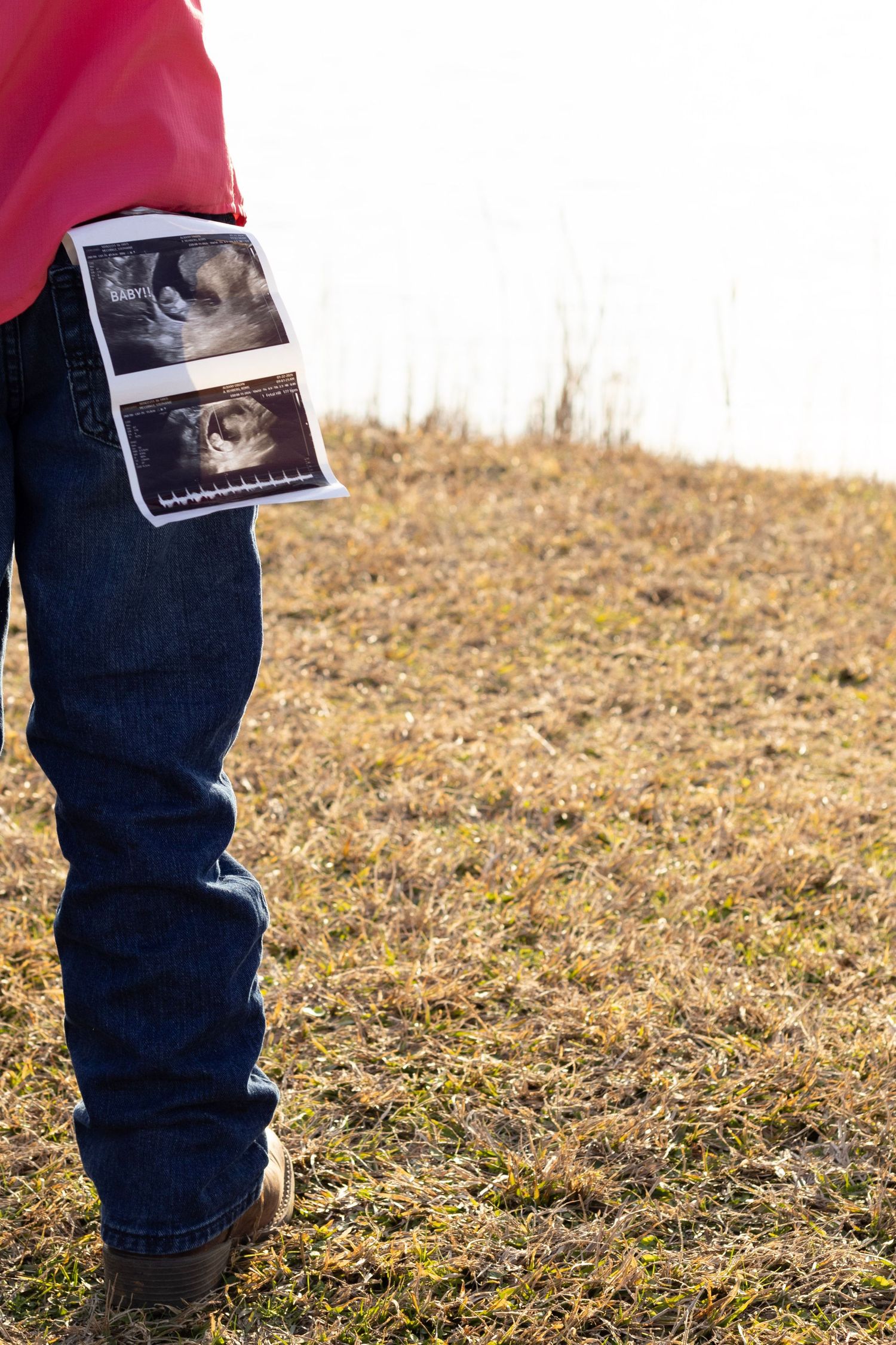 Child holding ultrasound photos while standing in a grassy field for pregnancy announcement.