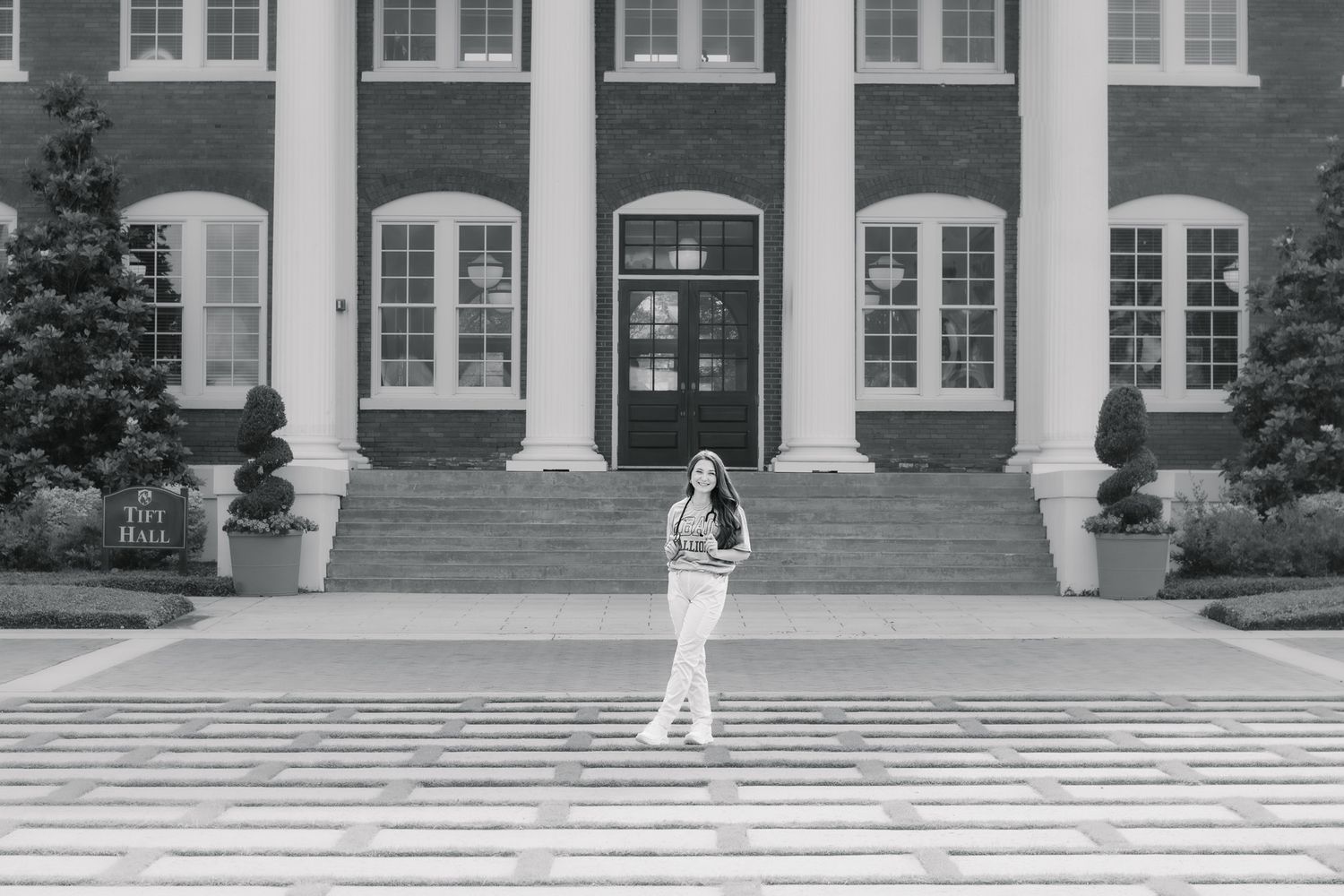 Young woman stands before a grand brick building with white columns in a black and white photo.