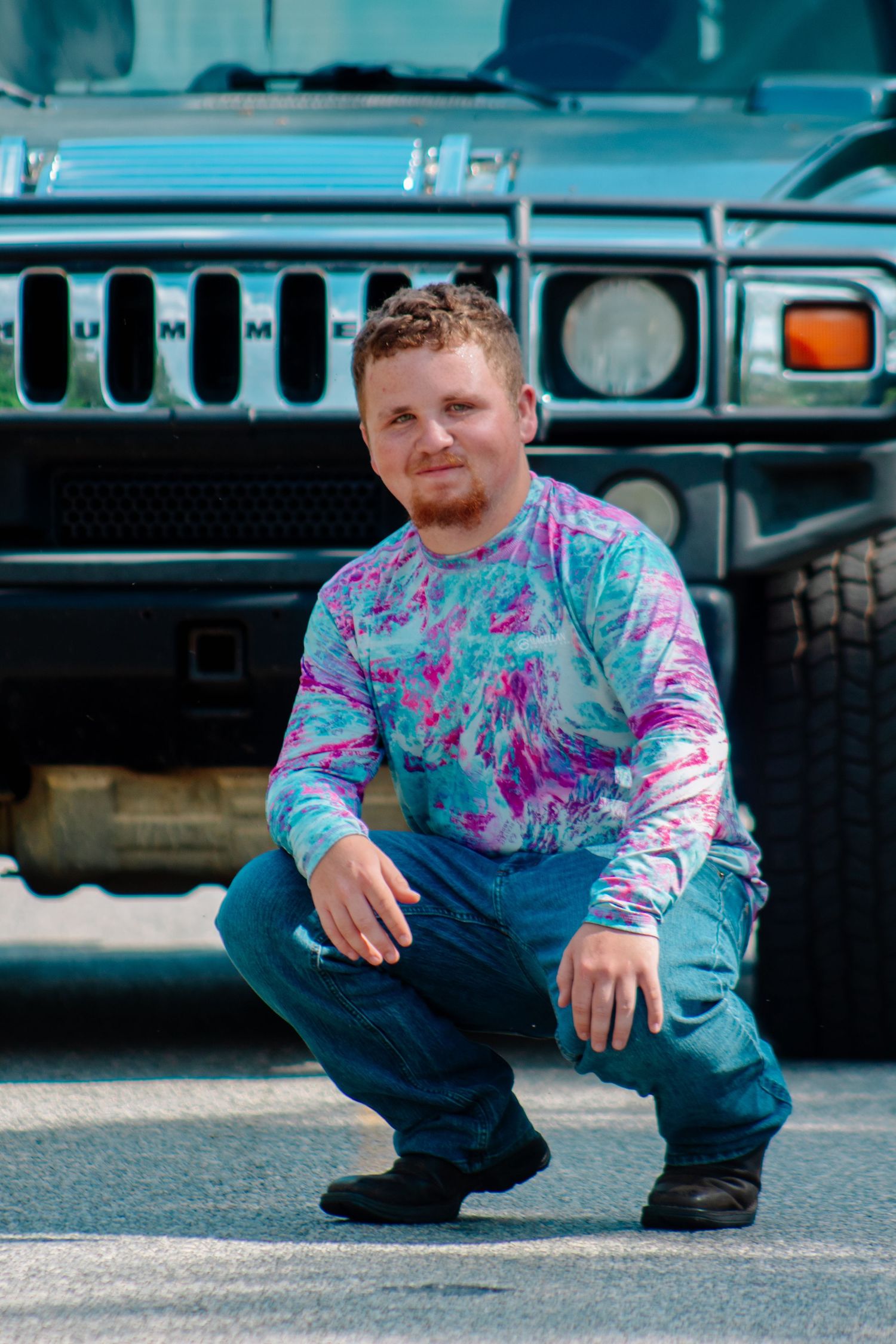 Man in tie-dye shirt crouching in front of a black Hummer H2 vehicle.