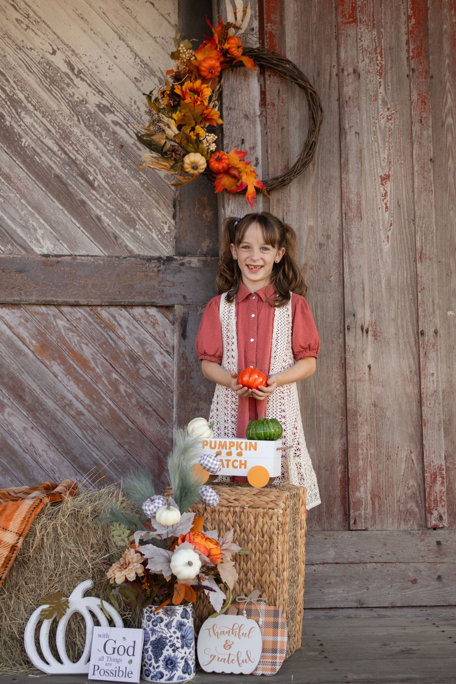 Young girl in red dress holding pumpkins at fall pumpkin patch barn photo session.