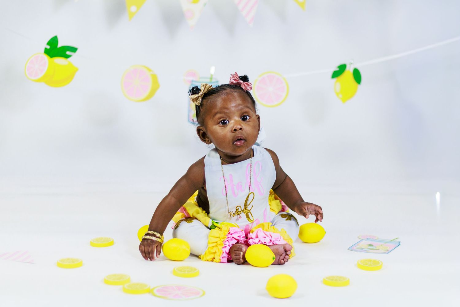 Adorable baby girl in yellow dress celebrating her first birthday with lemon-themed decorations.
