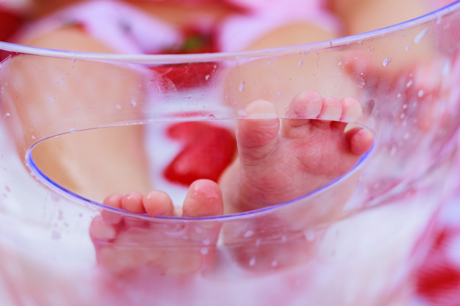Close-up of baby feet soaking in a clear bowl of water with rose petals.