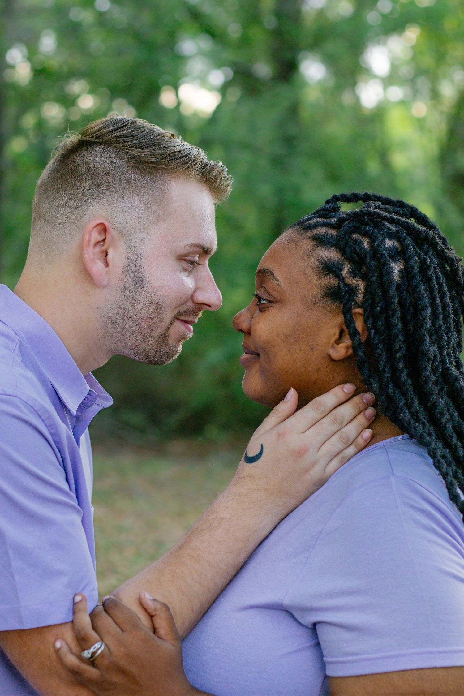 Interracial couple in matching lavender outfits share a romantic moment in lush green park.