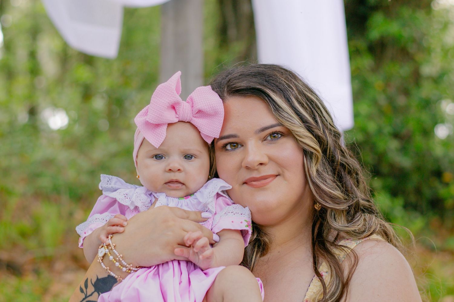 Mother and baby girl in matching pink outfits smiling together during outdoor spring photo session.