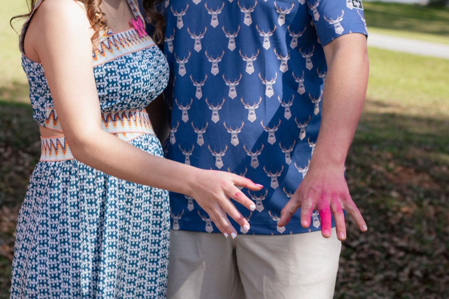 Close-up of couple holding hands with pink powder from gender reveal on fingers.