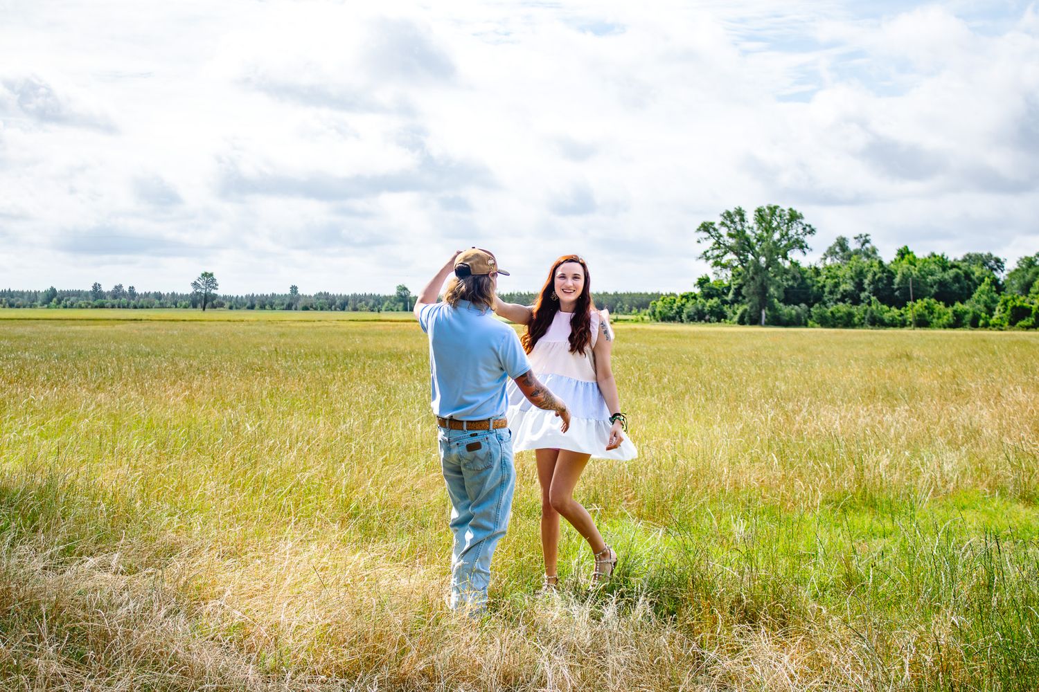 Couple dancing and holding hands in a wide open golden grassy field under a cloudy sky.