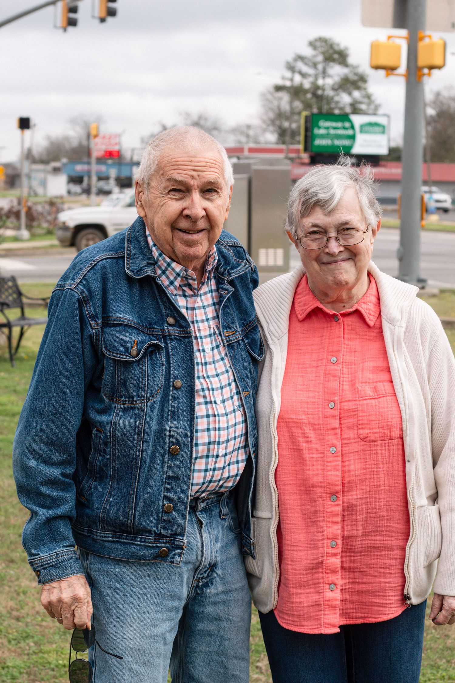 Smiling elderly couple standing together outdoors near a street intersection.