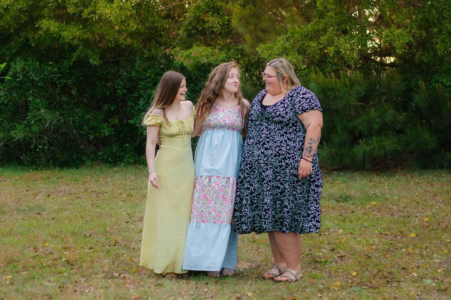 Three women in colorful dresses smiling together outdoors in a green park setting.