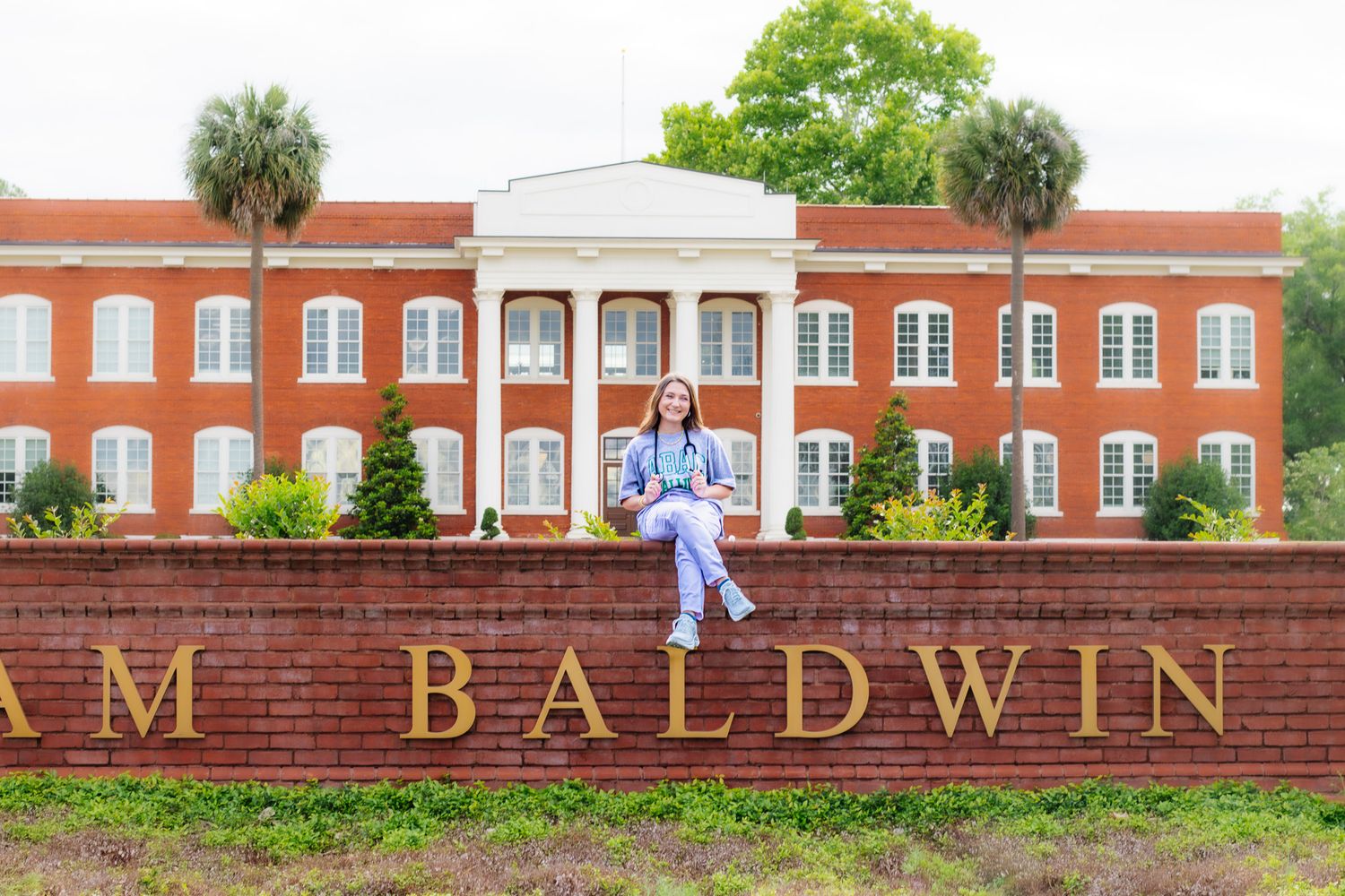 Student sits on brick Baldwin university sign in front of red brick building.