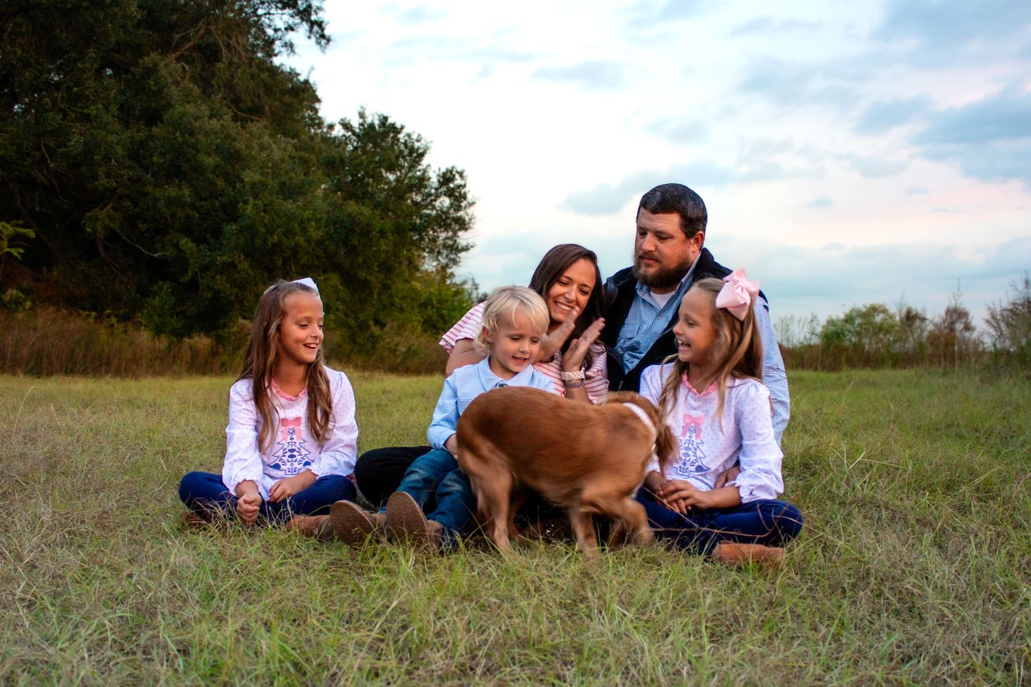 Joyful family of five laughing with their Spaniel dog in an open field.