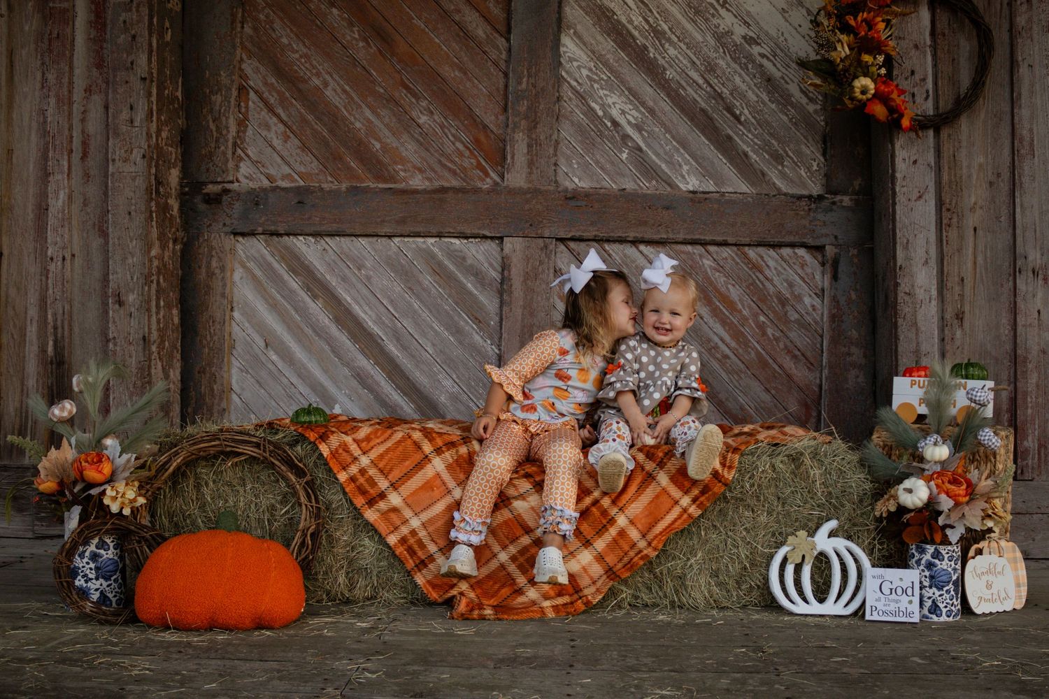 Two little sisters sharing a sweet kiss on hay bale during fall barn photo session.