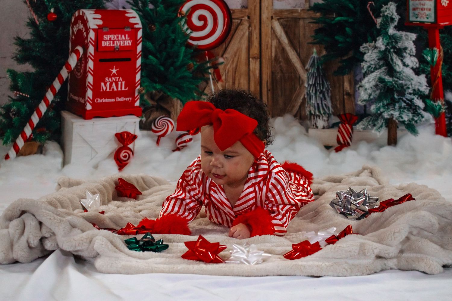 Baby in red and white striped outfit lying on blanket in a Christmas mail holiday photo backdrop.