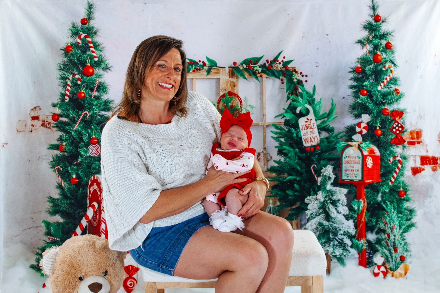Woman in white sweater holds newborn in red Christmas outfit during festive holiday photo session.