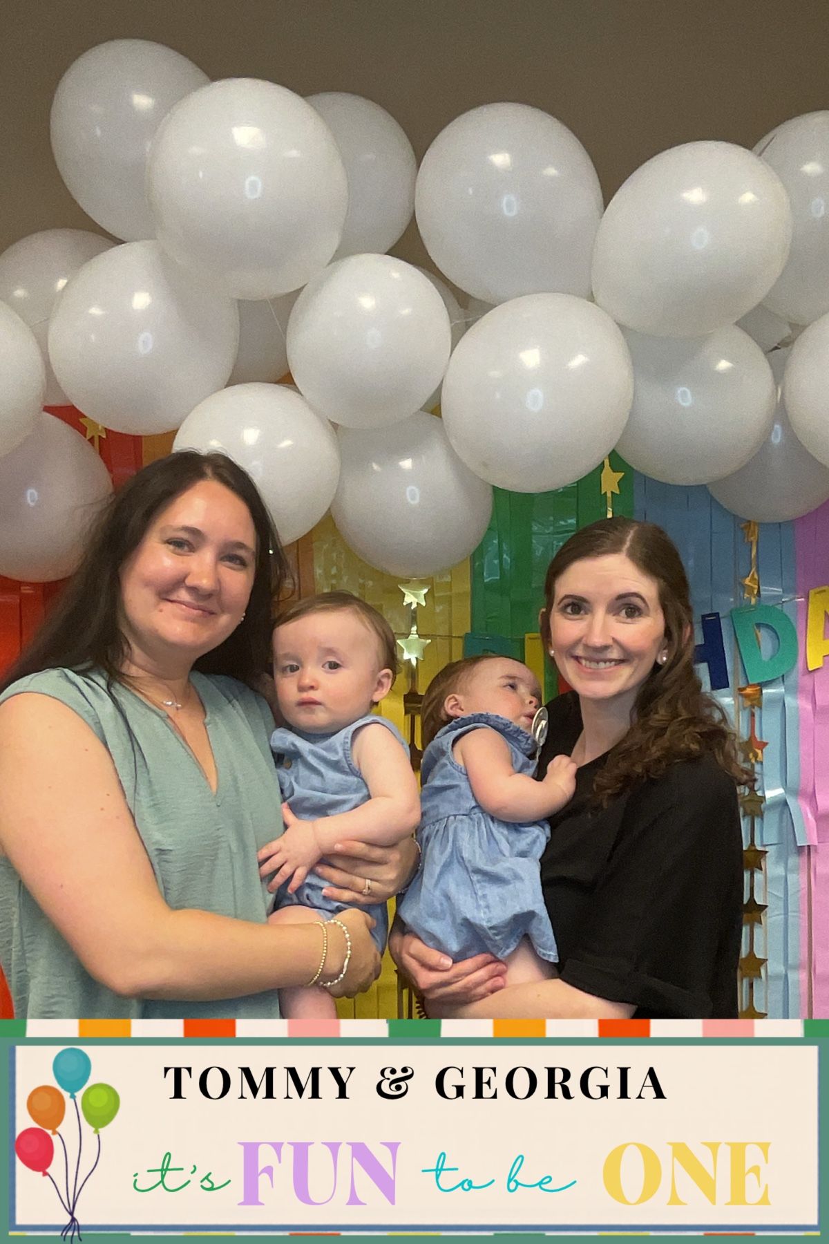 Two women holding twin babies at a first birthday party with white balloons and colorful decorations for Tommy and Georgia.