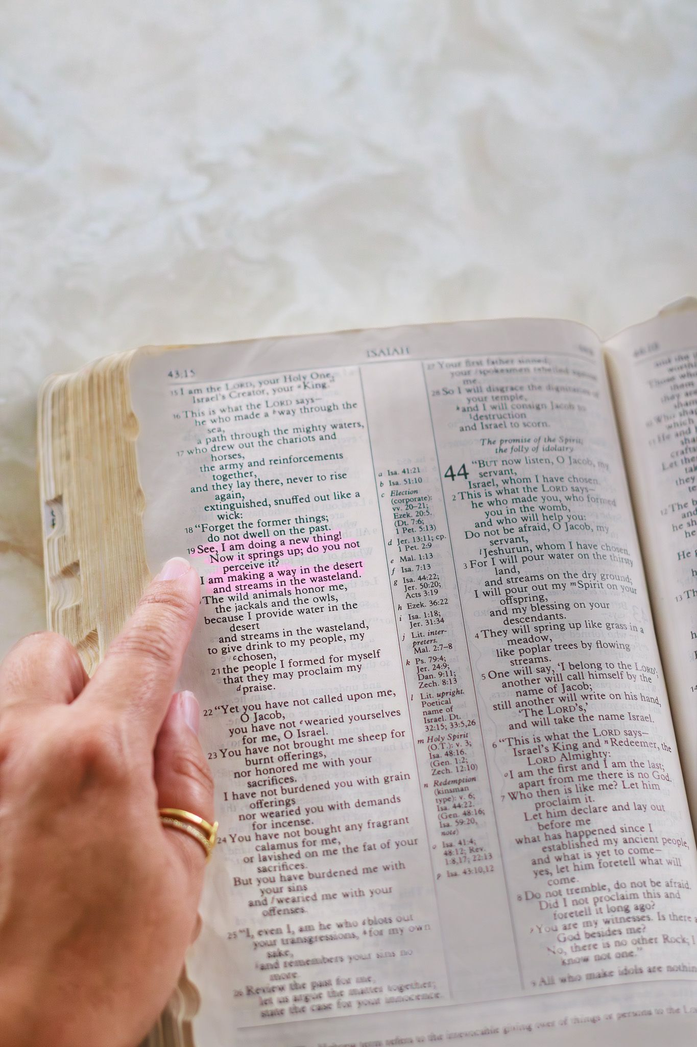 Hand pointing to highlighted verse in open Bible with gold wedding ring, religious study and scripture reading concept.