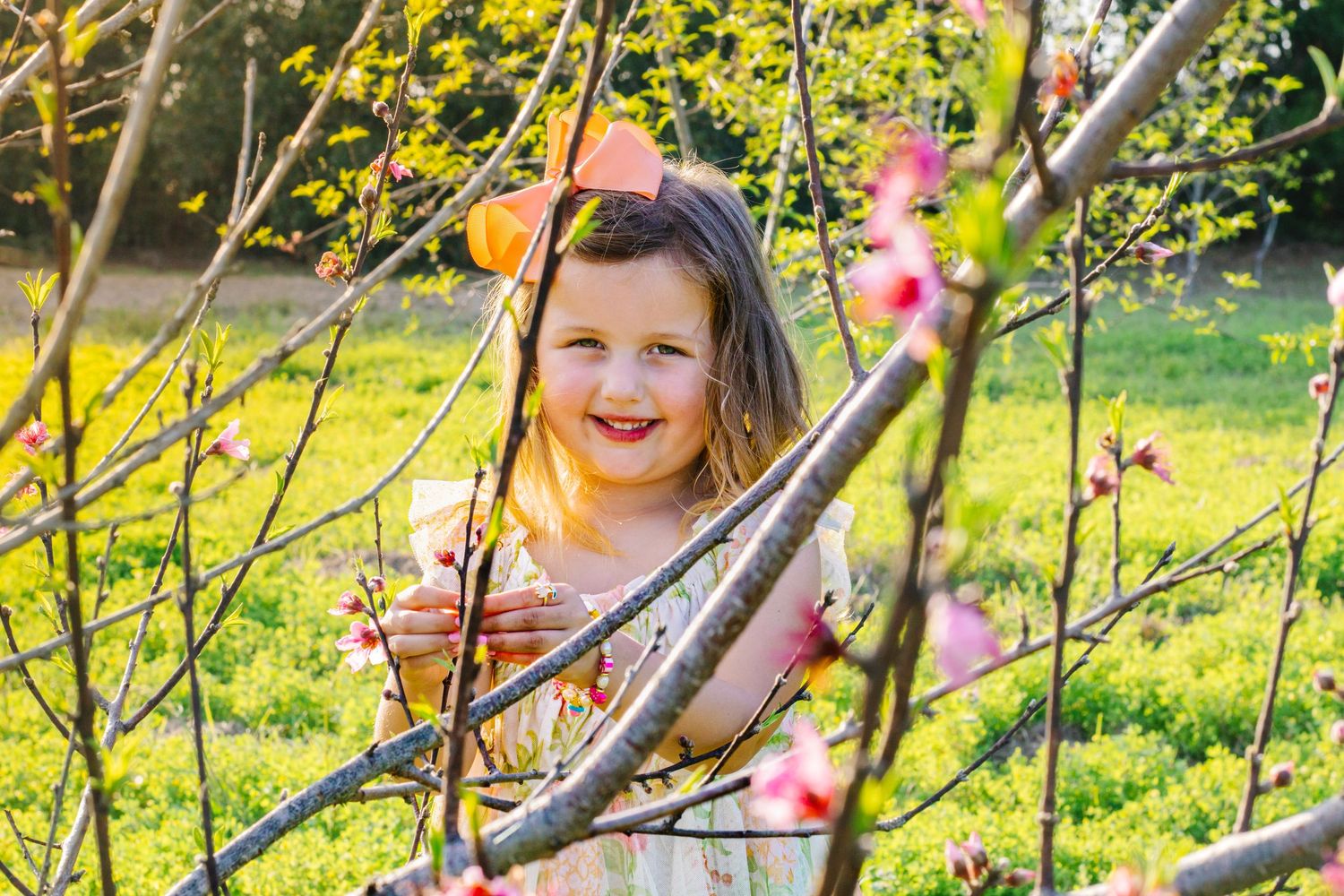 Cheerful little girl laughing among pink spring blossoms in a sunlit garden setting.