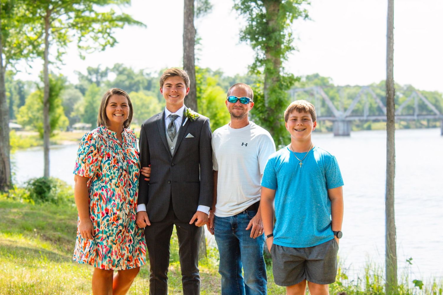 Family of four poses outdoors near a river, with one young man dressed in a suit for a formal occasion.
