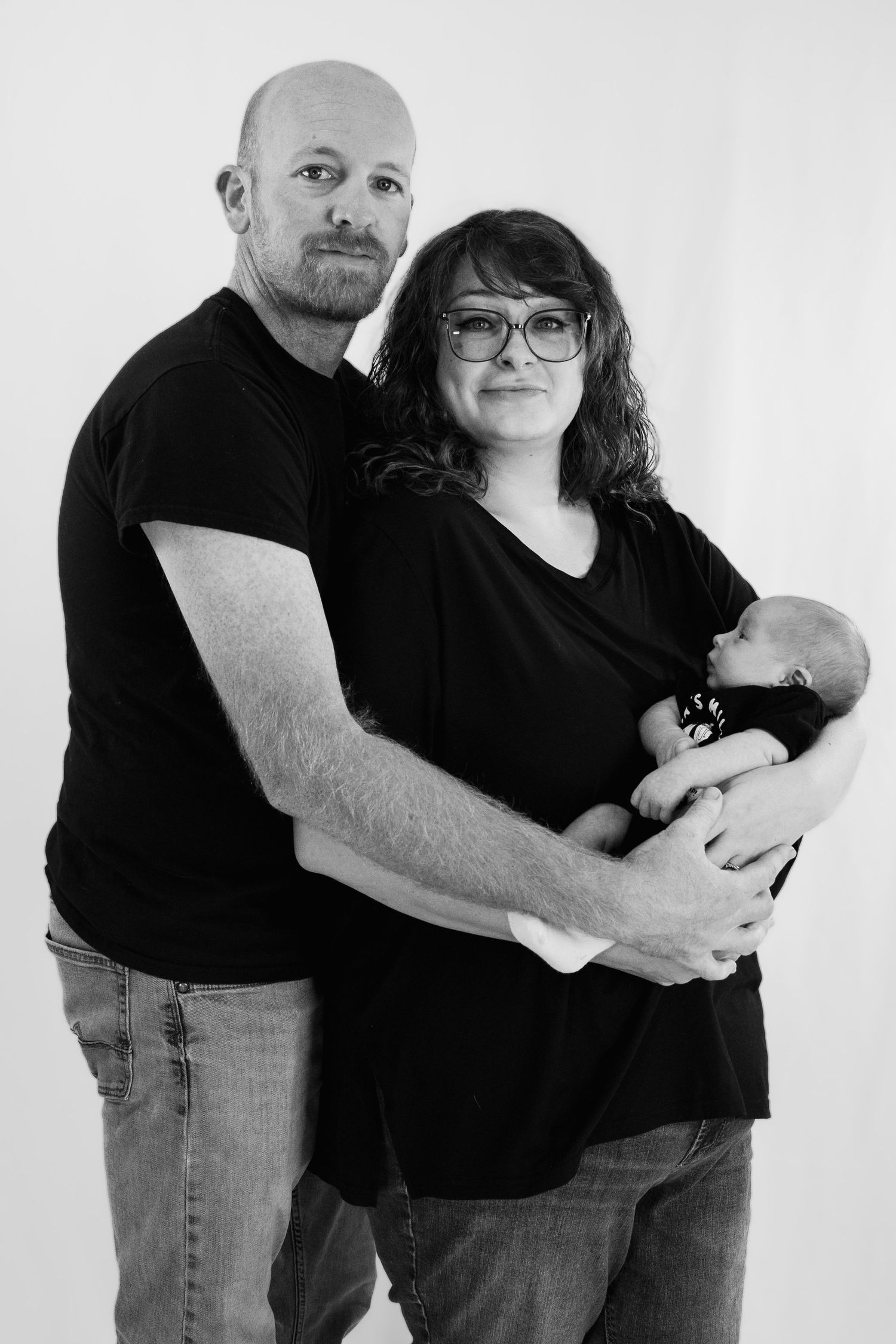 Black and white portrait of parents in matching black shirts tenderly holding their newborn baby.